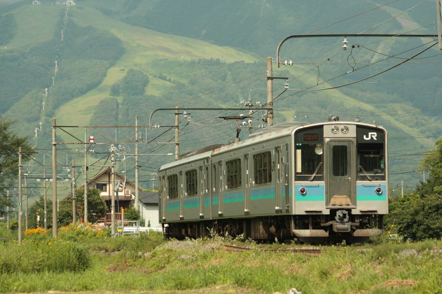 Tren JR que circula con montañas verdes de fondo y paisaje circundante