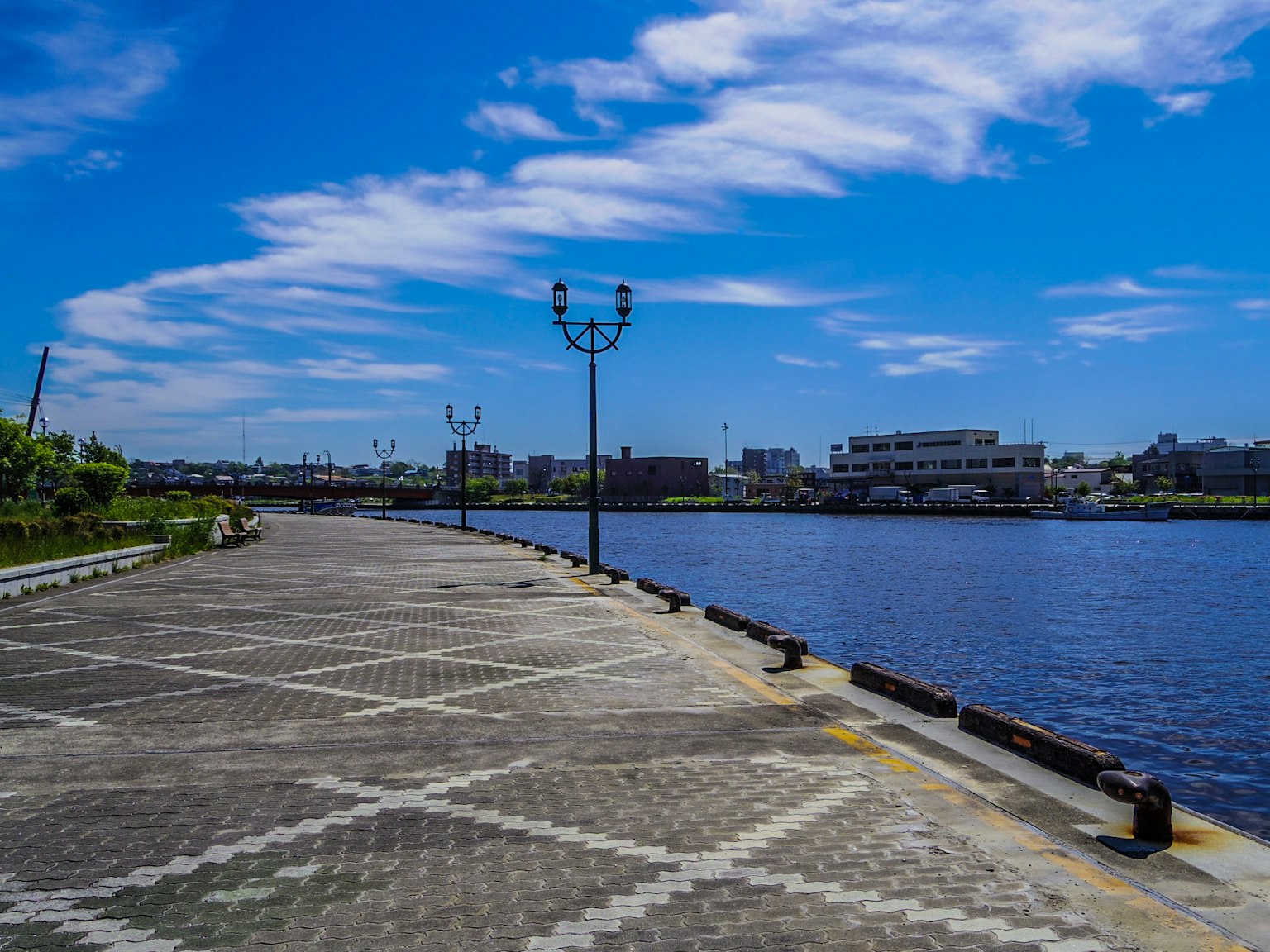 Passeggiata pavimentata lungo il fiume sotto un cielo blu con nuvole sparse