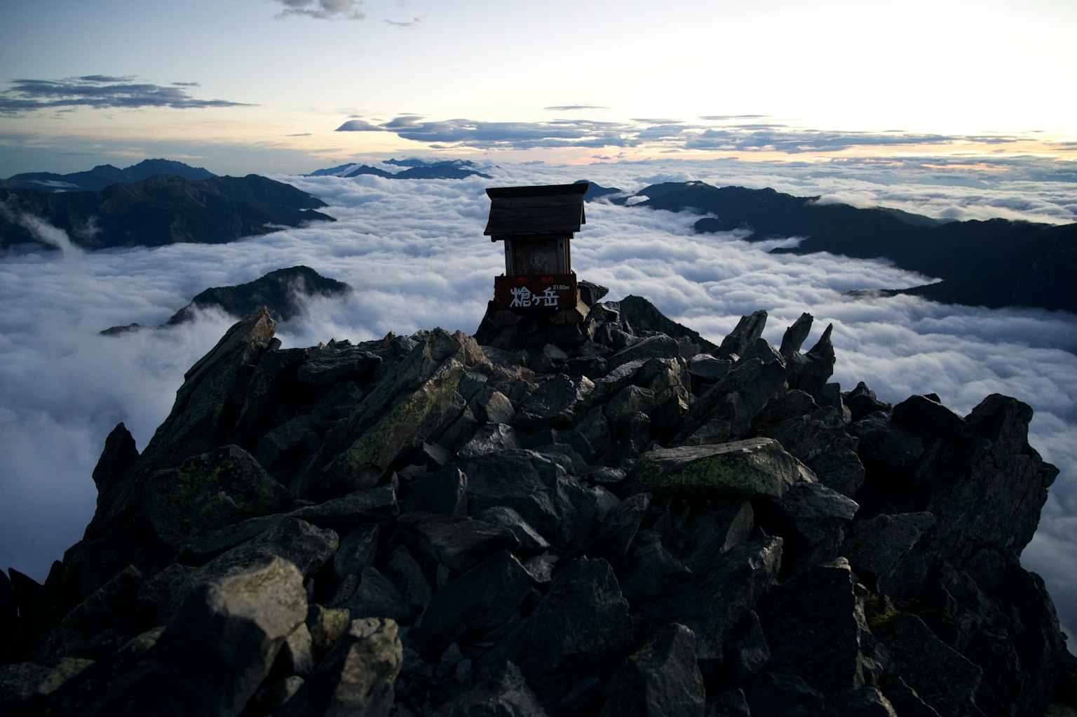 Berggipfel mit einer kleinen Hütte umgeben von Wolken und Felsen
