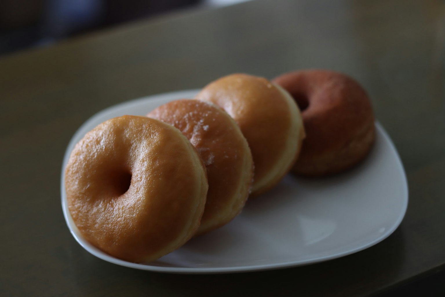 Foto von Donuts auf einem Teller drei einfache Donuts und ein Schokoladendonut sichtbar