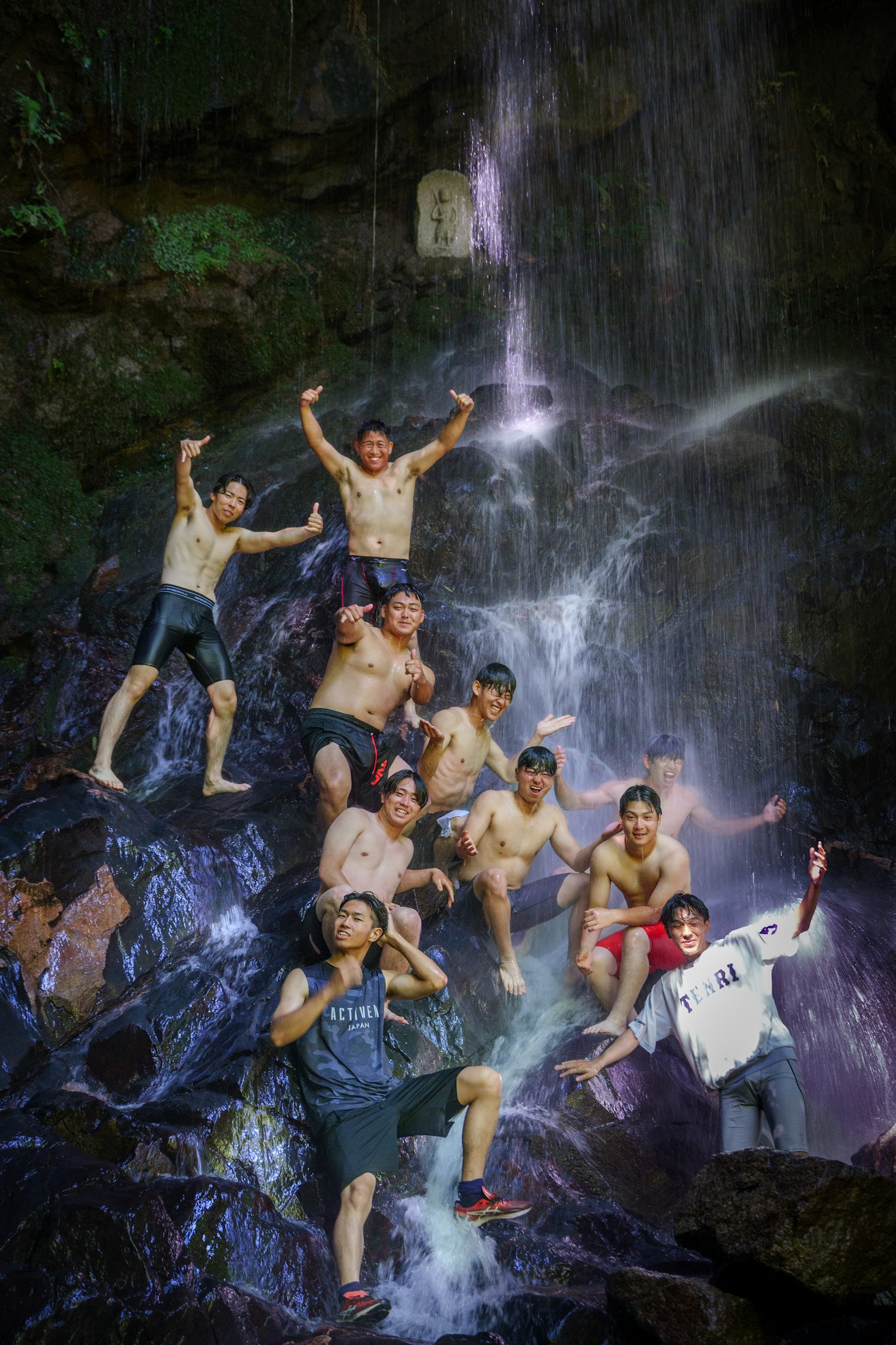 Gruppo di giovani che giocano vicino a una cascata spruzzando acqua e arrampicandosi sulle rocce