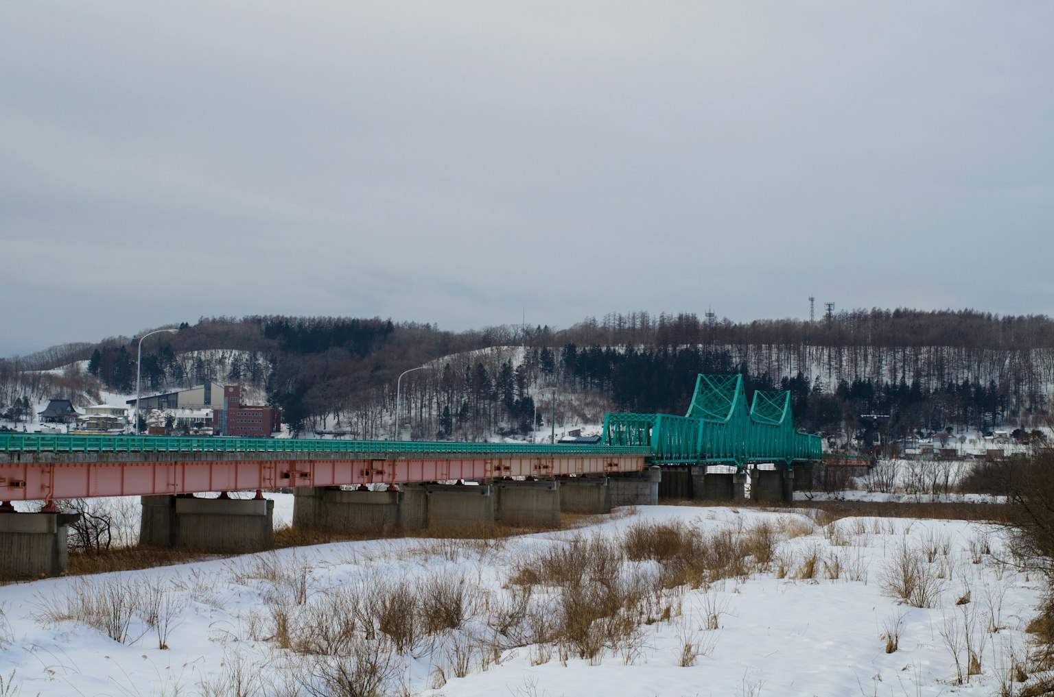 Blue bridge over snowy landscape with hills in the background