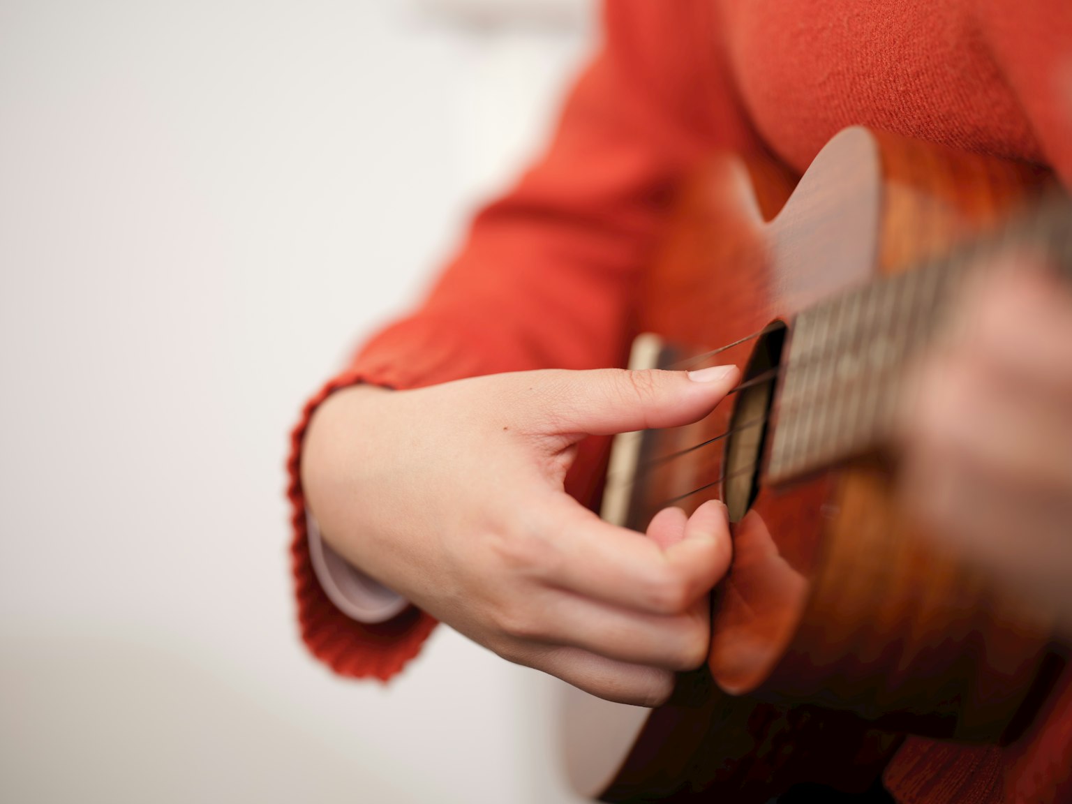 Kedekatan tangan bermain ukulele mengenakan sweter merah