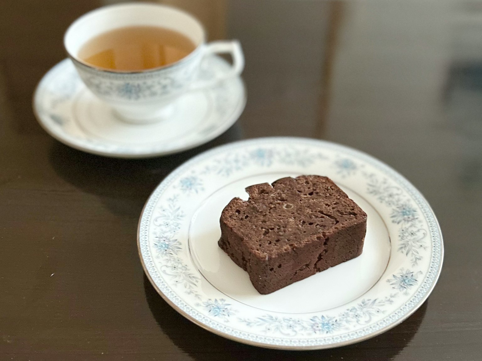 Ein Teller mit Brownie und einer Tasse Tee auf einem Holztisch