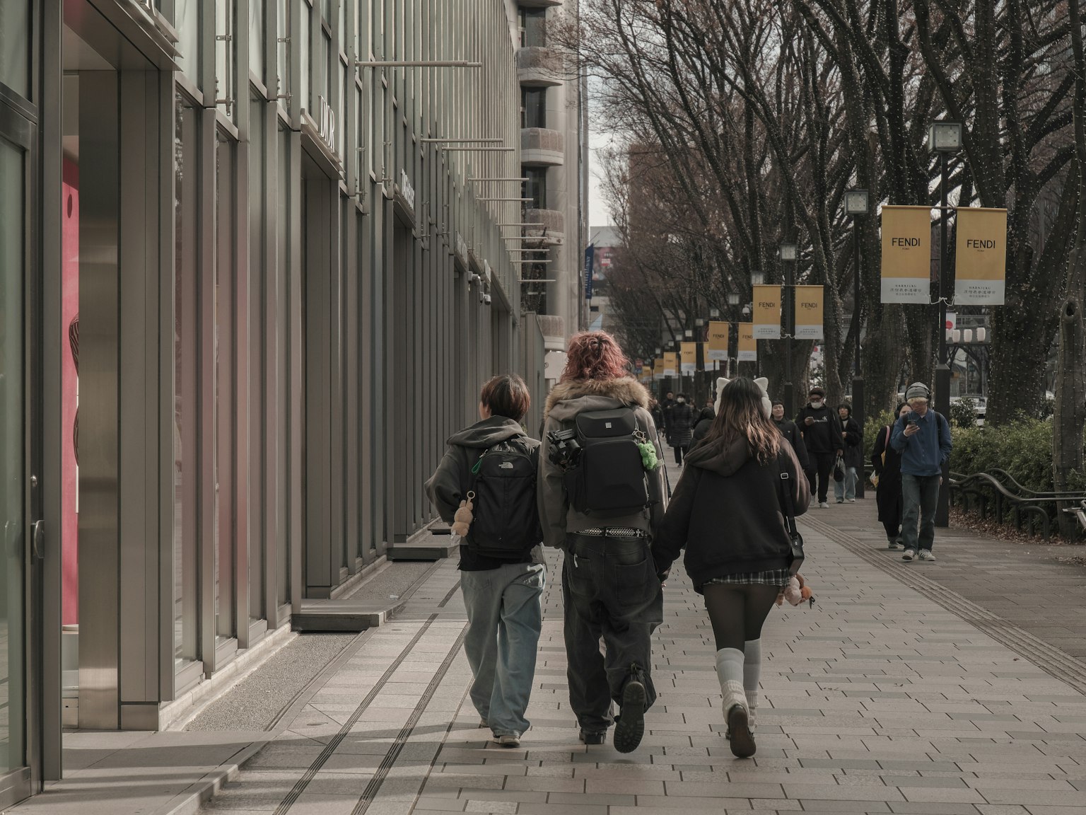 Personas caminando en un entorno urbano con escaparates y árboles a lo largo de la calle