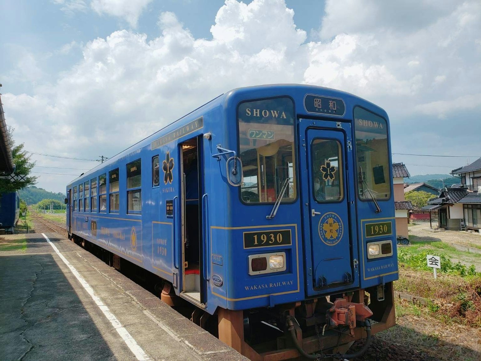Ein blauer Zug steht an einem Bahnhof unter einem bewölkten Himmel
