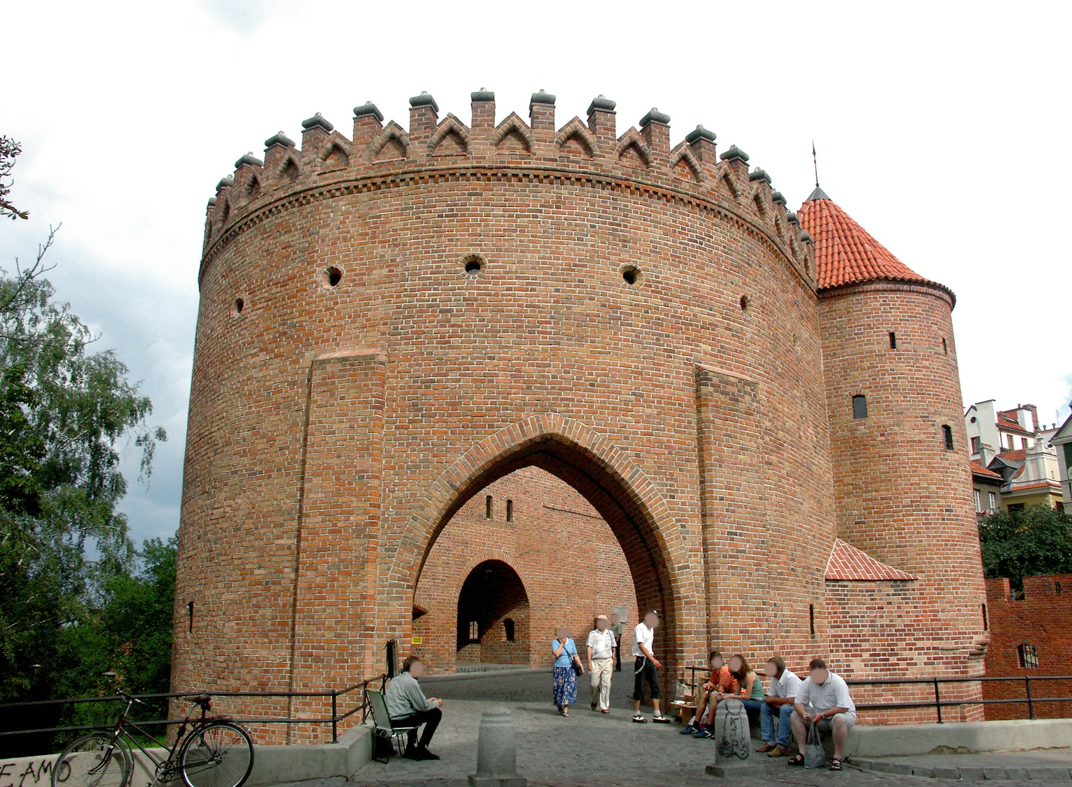 Tour médiévale en brique avec créneaux et arches entourée de personnes