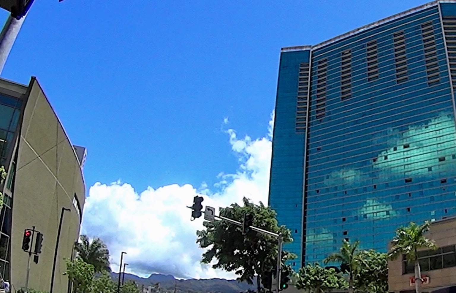 Paisaje urbano con un edificio verde y un rascacielos de vidrio bajo un cielo azul con nubes