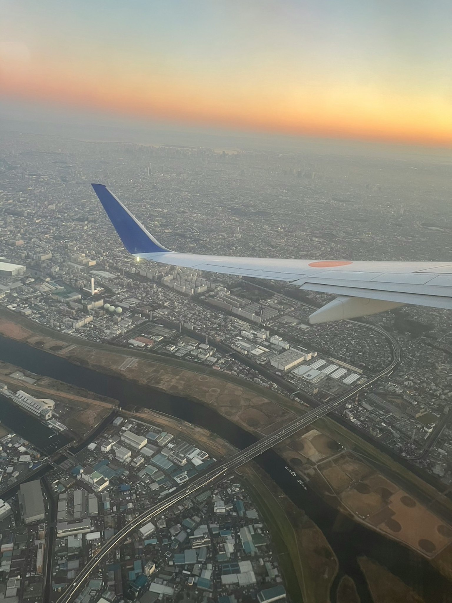 Ala di un aereo con paesaggio urbano sotto un cielo al tramonto