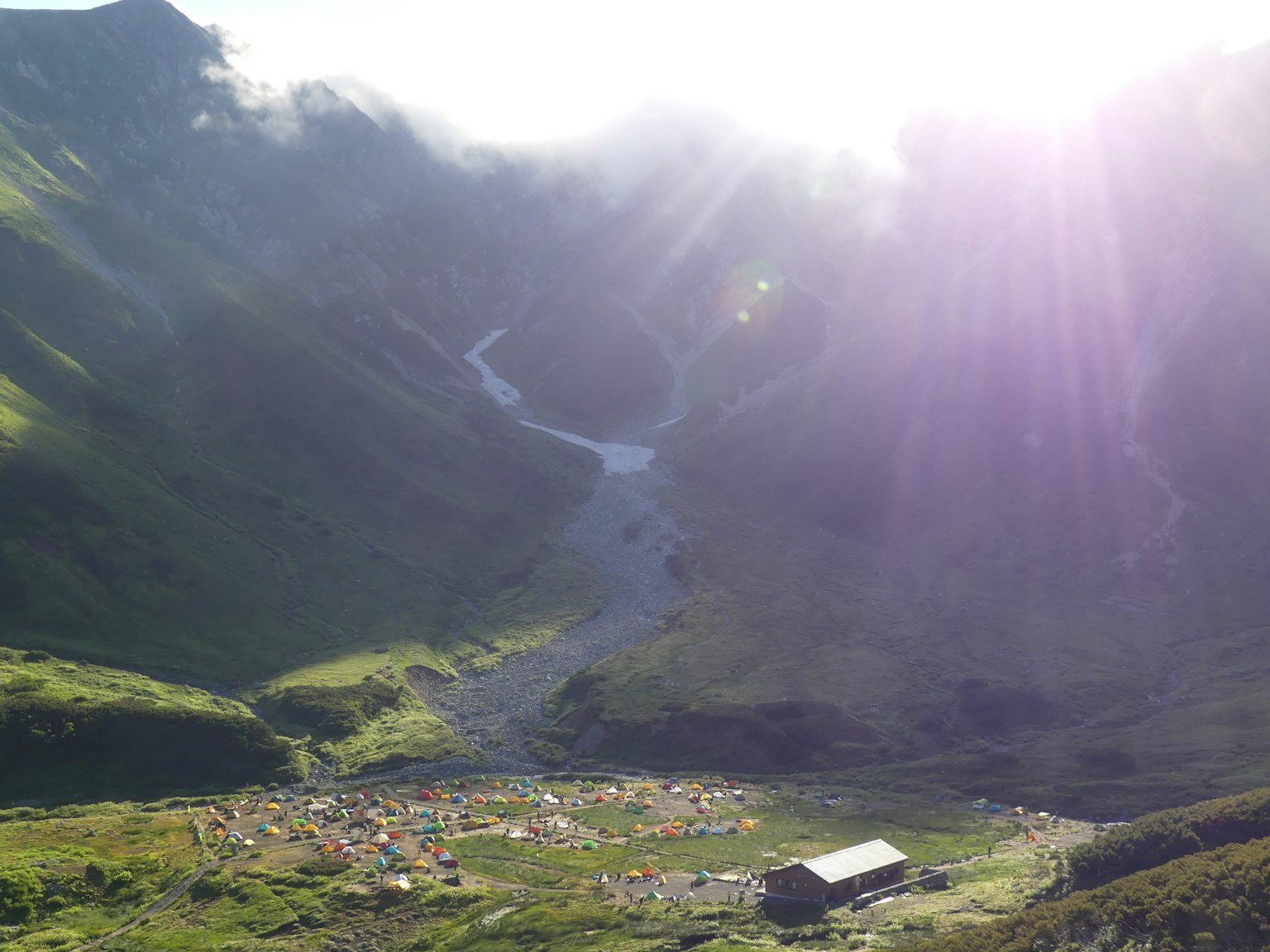 Lebhafte Tal mit verstreuten Zelten und einer Hütte, die im Sonnenlicht erstrahlt