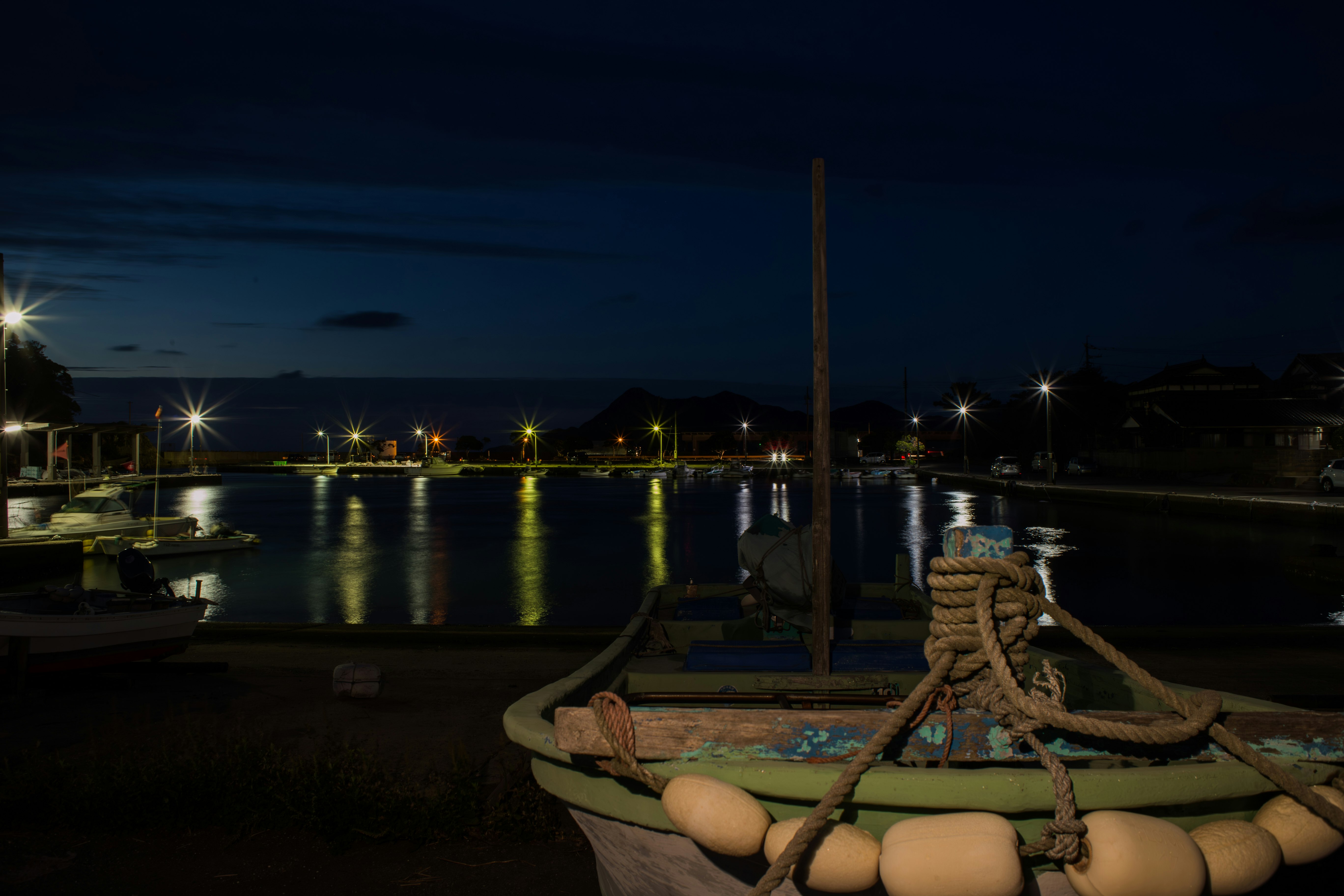 night harbor scene with a moored rowboat and reflections on the water
