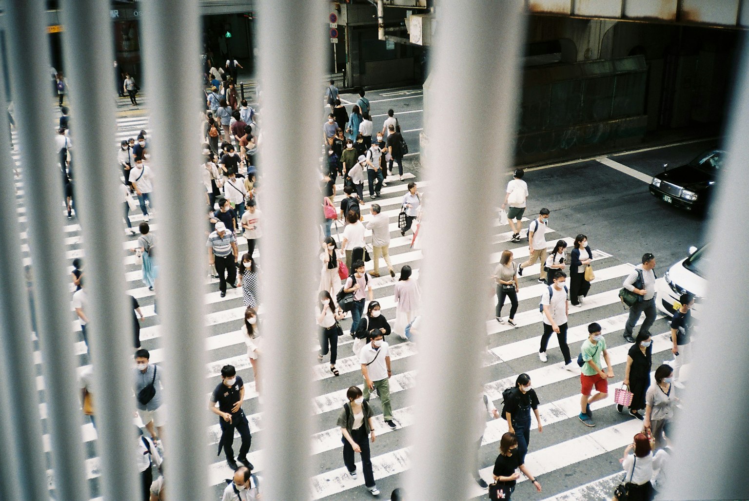 Image capturing people crossing a pedestrian crosswalk viewed through vertical white barriers