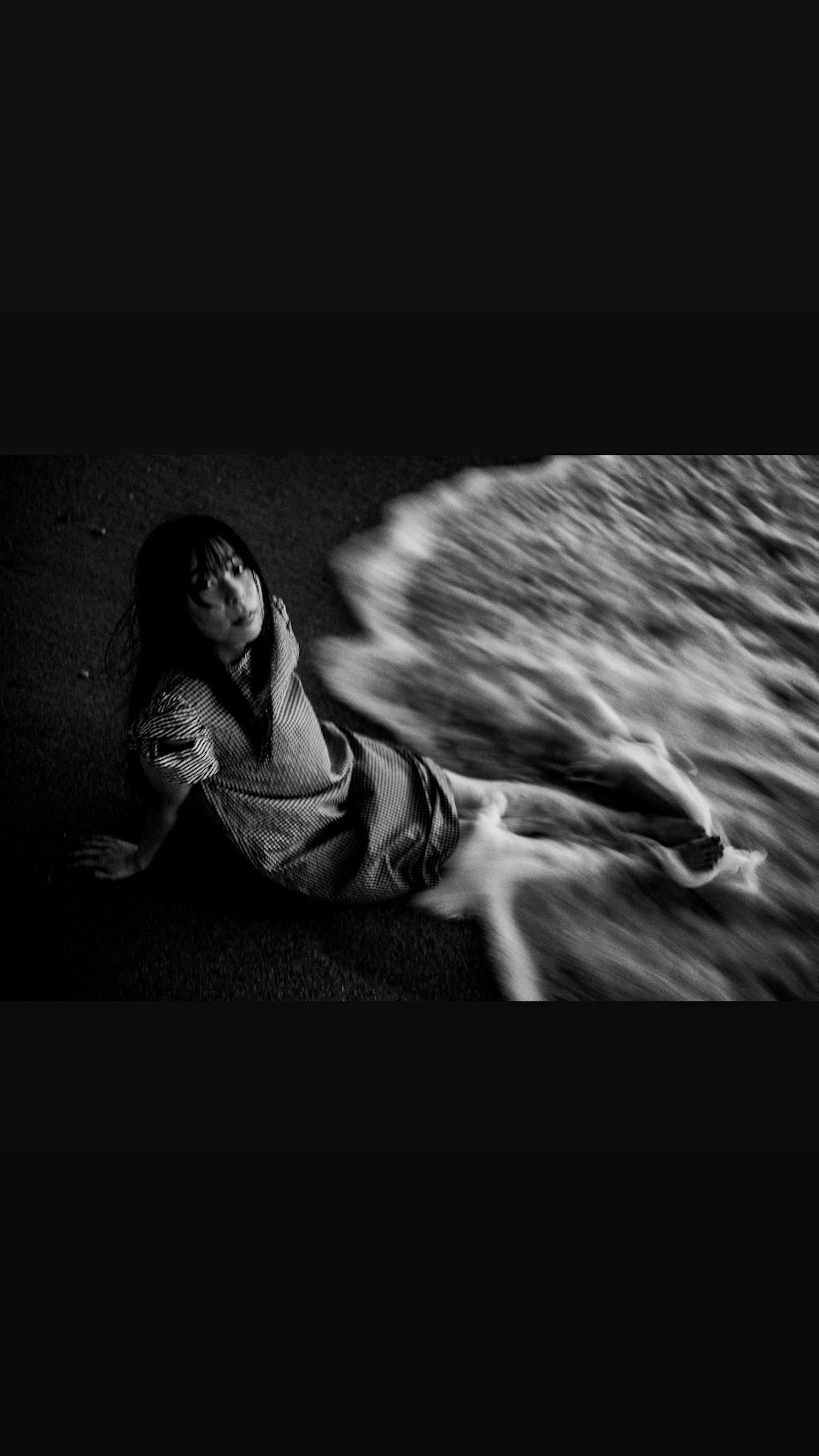 Black and white photo of a girl lying by the shore