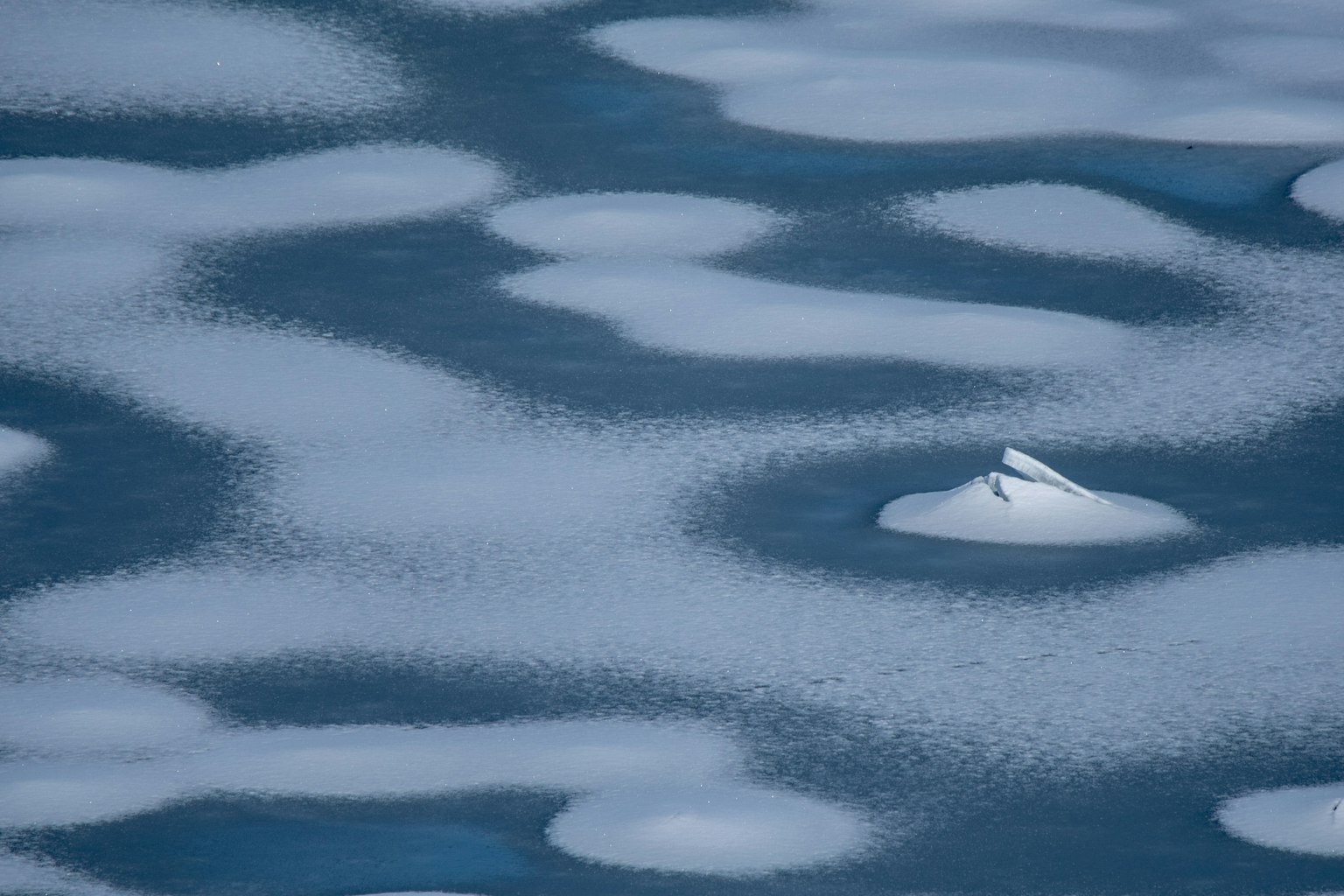 Muster von Schnee auf einer kalten blauen Wasseroberfläche mit Eisformationen
