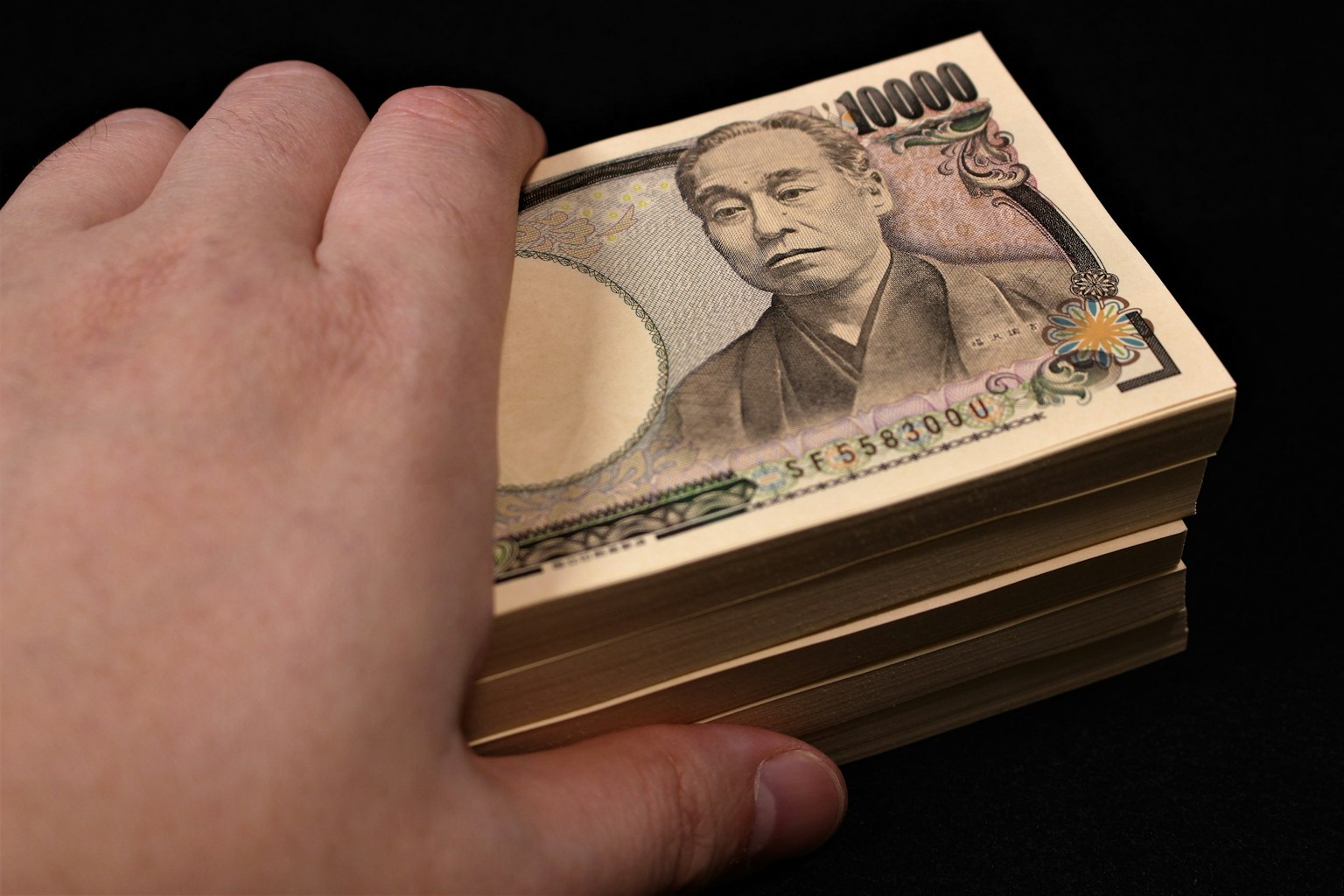 Una mano che tiene una pila di banconote giapponesi con un focus su una banconota da 10000 yen su sfondo nero