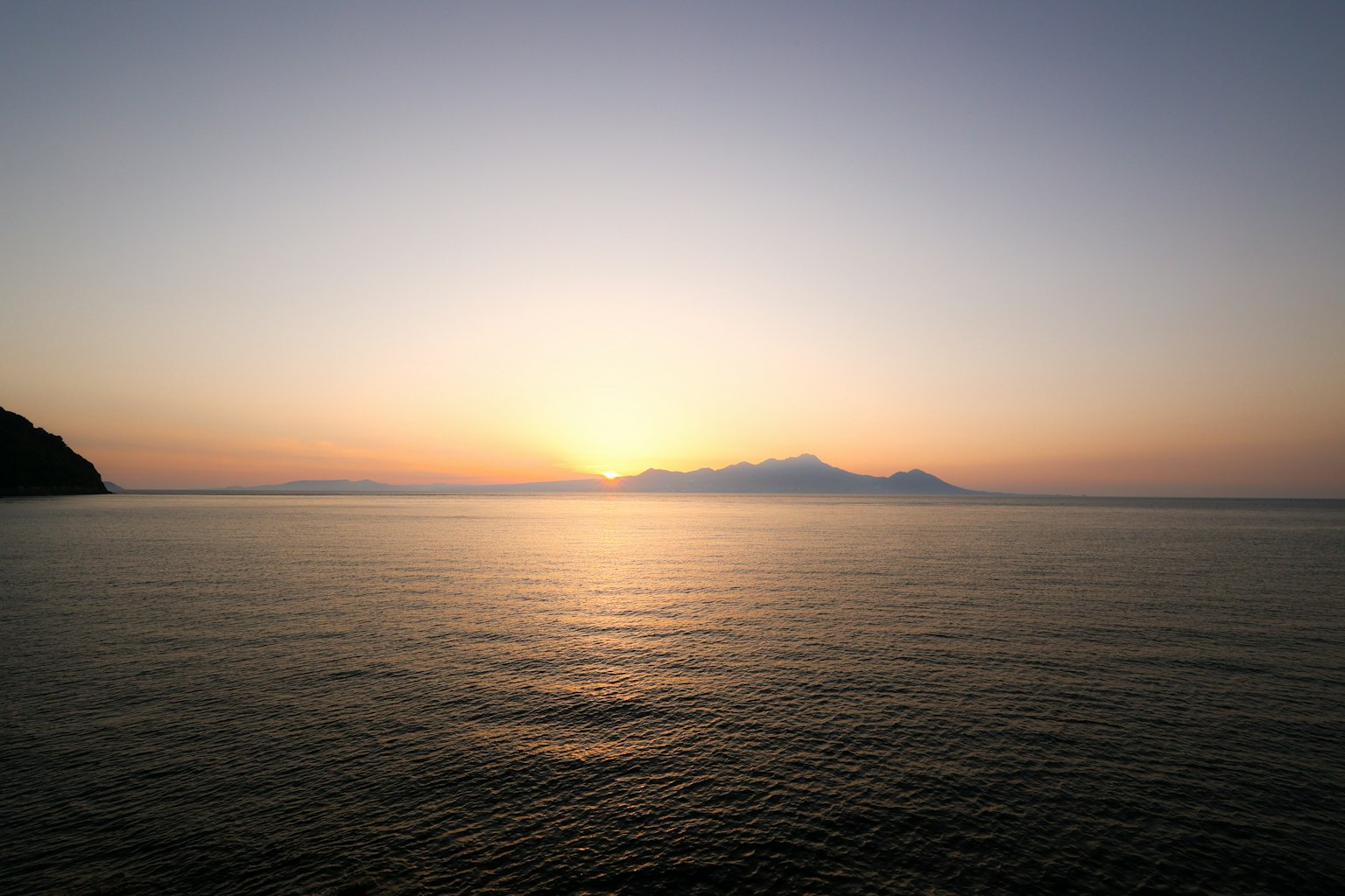 Mar tranquilo con un sol poniente y islas distantes