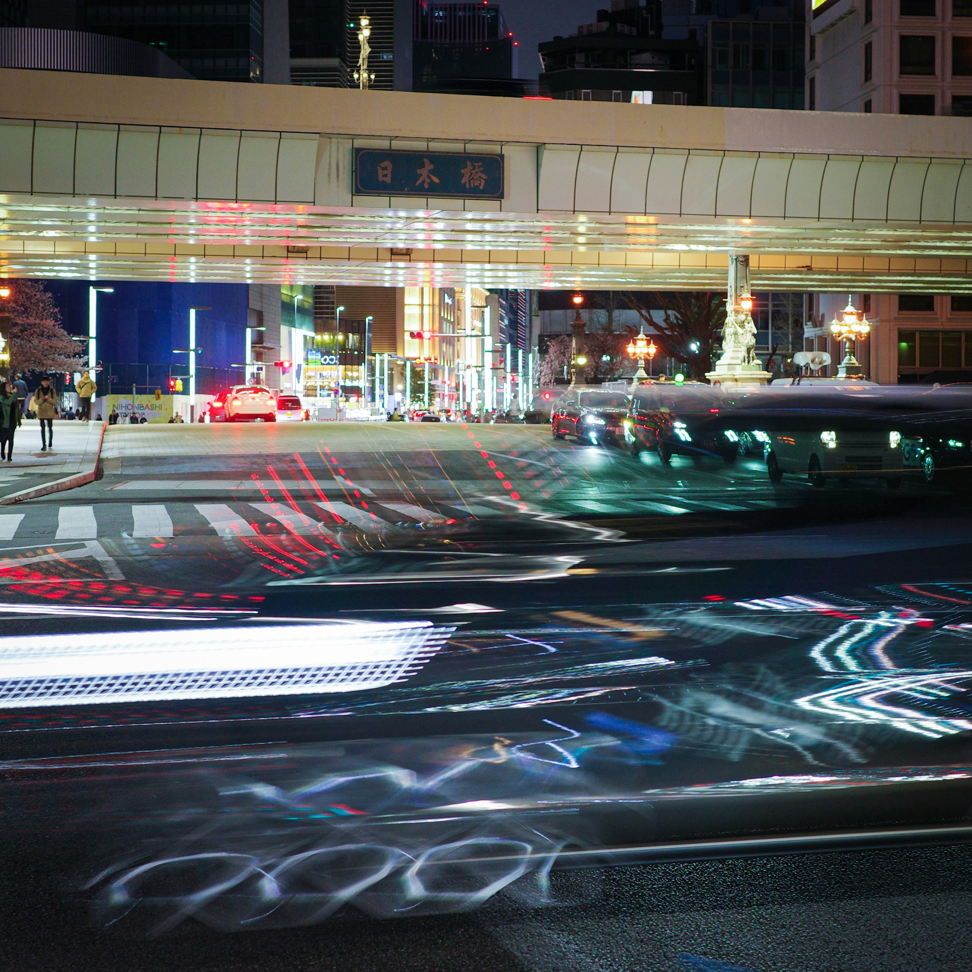日本橋の夜の交差点を流れる車の光跡