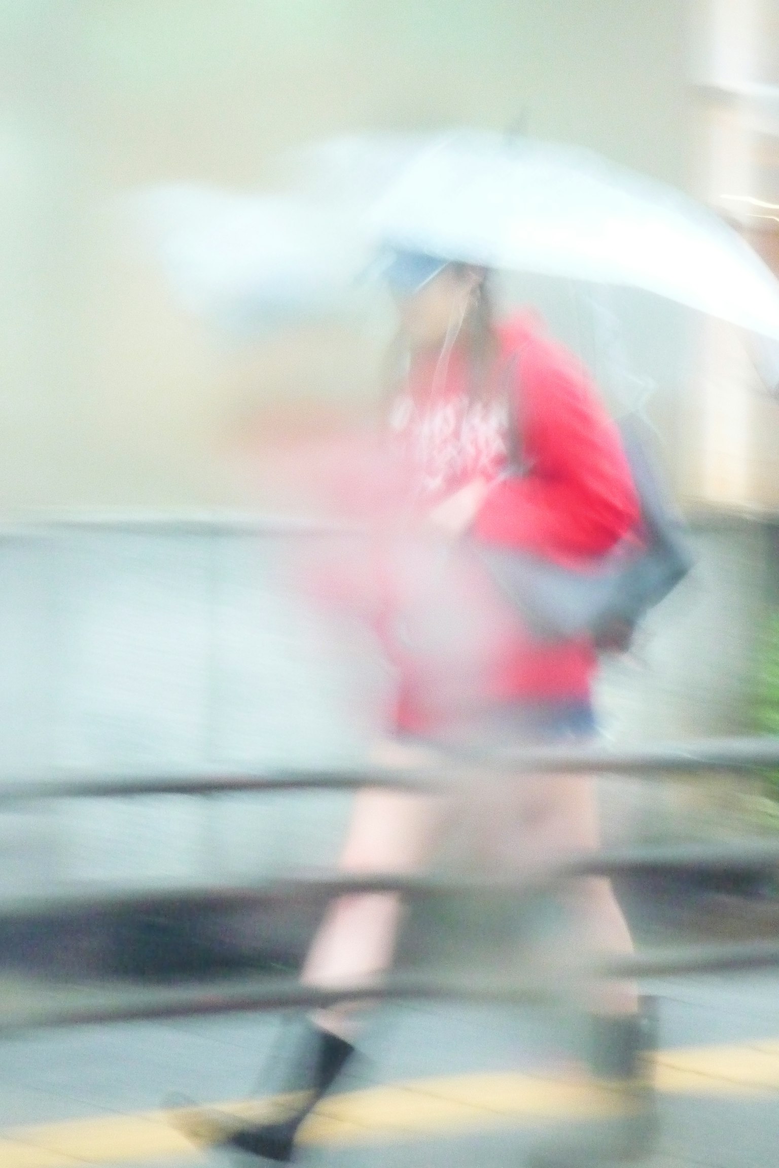Blurry image of a person walking with an umbrella wearing a red outfit and boots