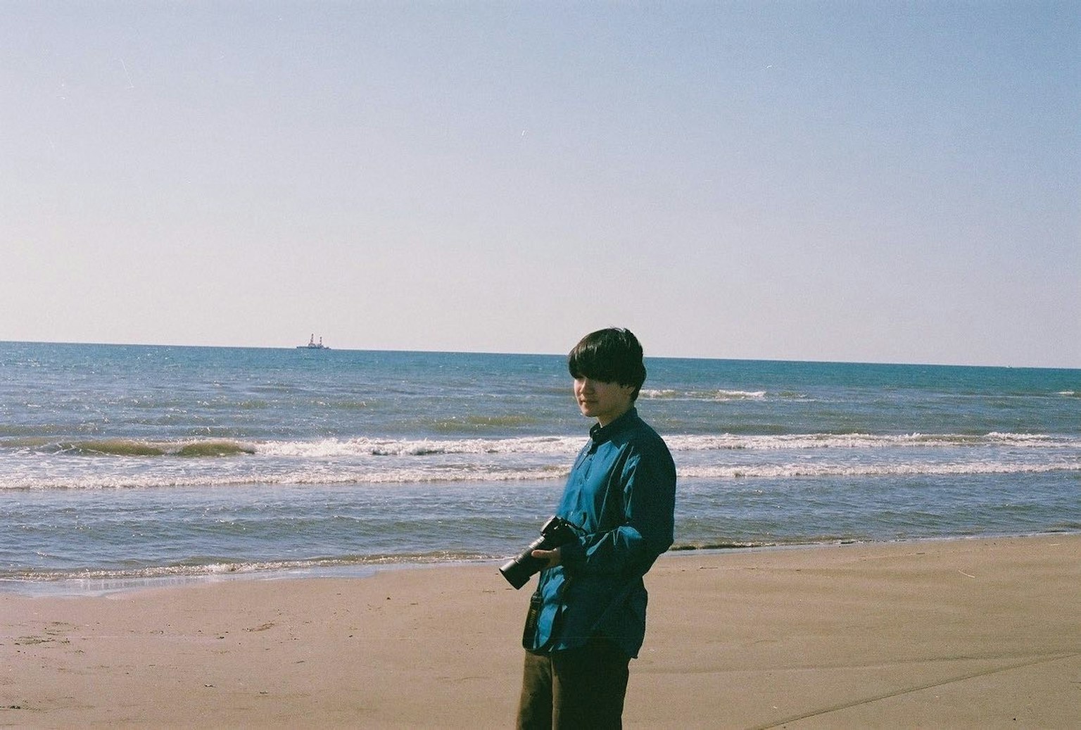 คนถือกล้องที่ชายหาดสวมแจ็คเก็ตสีน้ำเงินและหมวกสีดำ