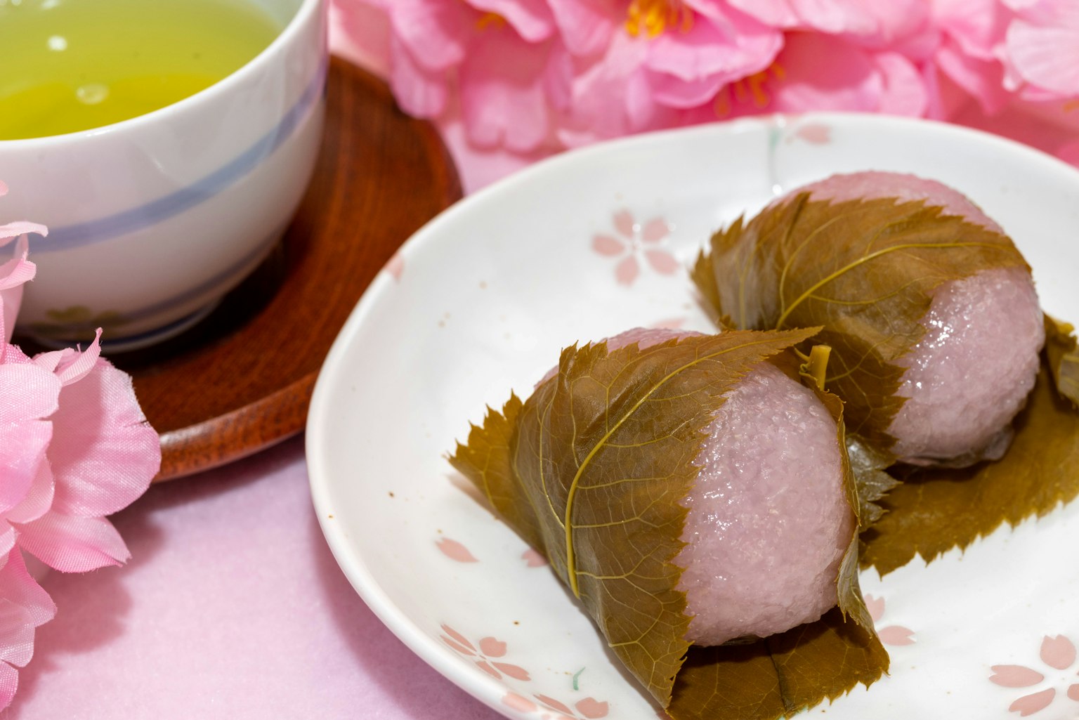 배경에 벚꽃이 있는 접시 위의 사쿠라 모찌와 녹차 한 잔