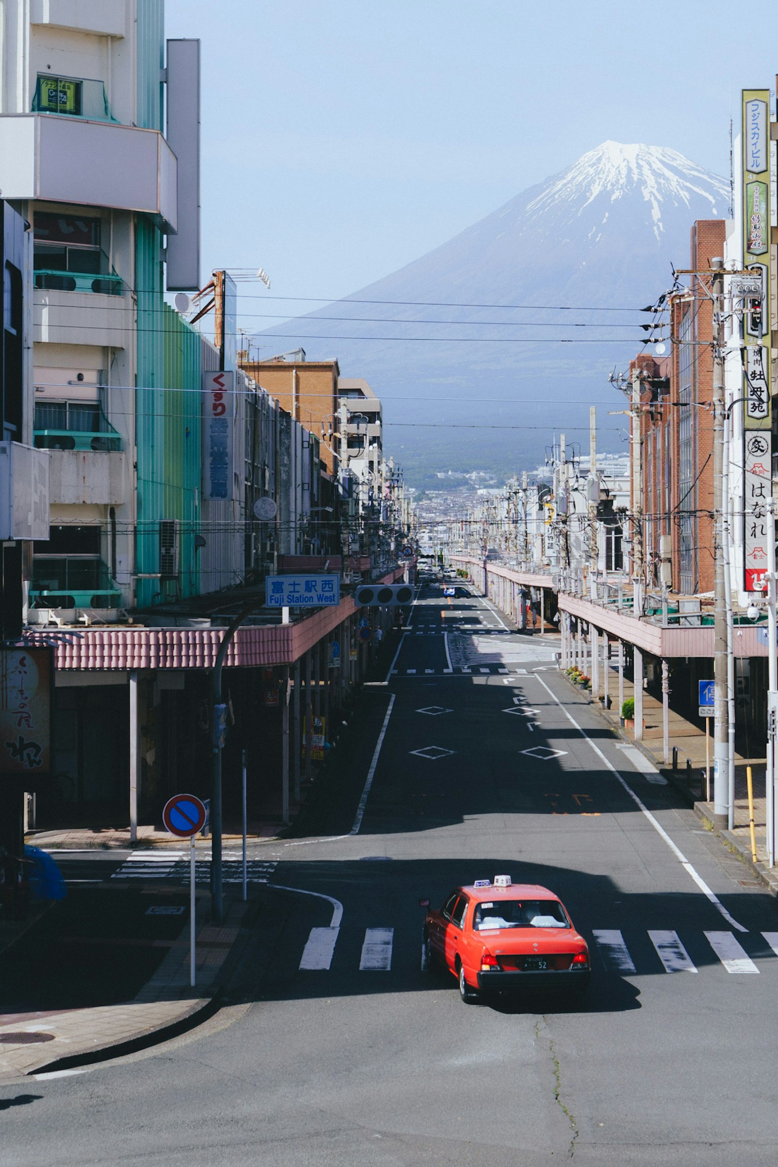 A red car driving through a street with Mount Fuji in the background