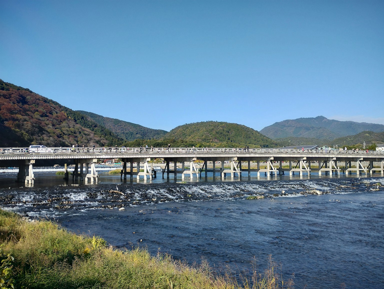 ทิวทัศน์ของสะพานข้ามแม่น้ำใต้ท้องฟ้าสีฟ้าพร้อมภูเขาสีเขียวในพื้นหลัง
