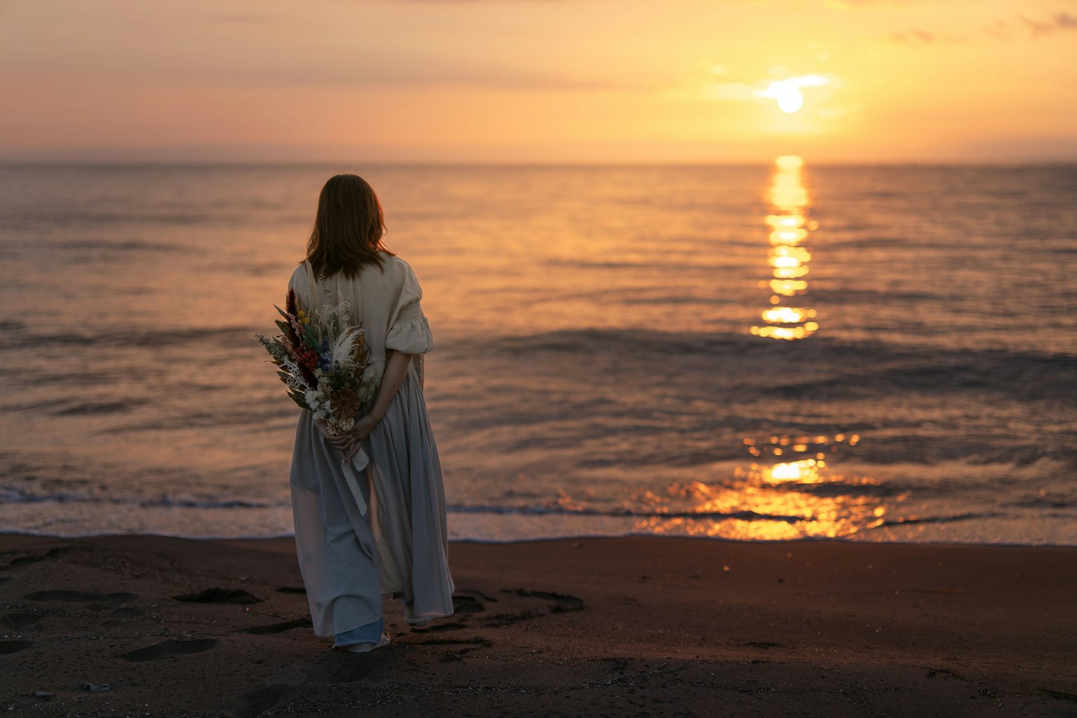 A woman standing by the beach with the sunset in the background
