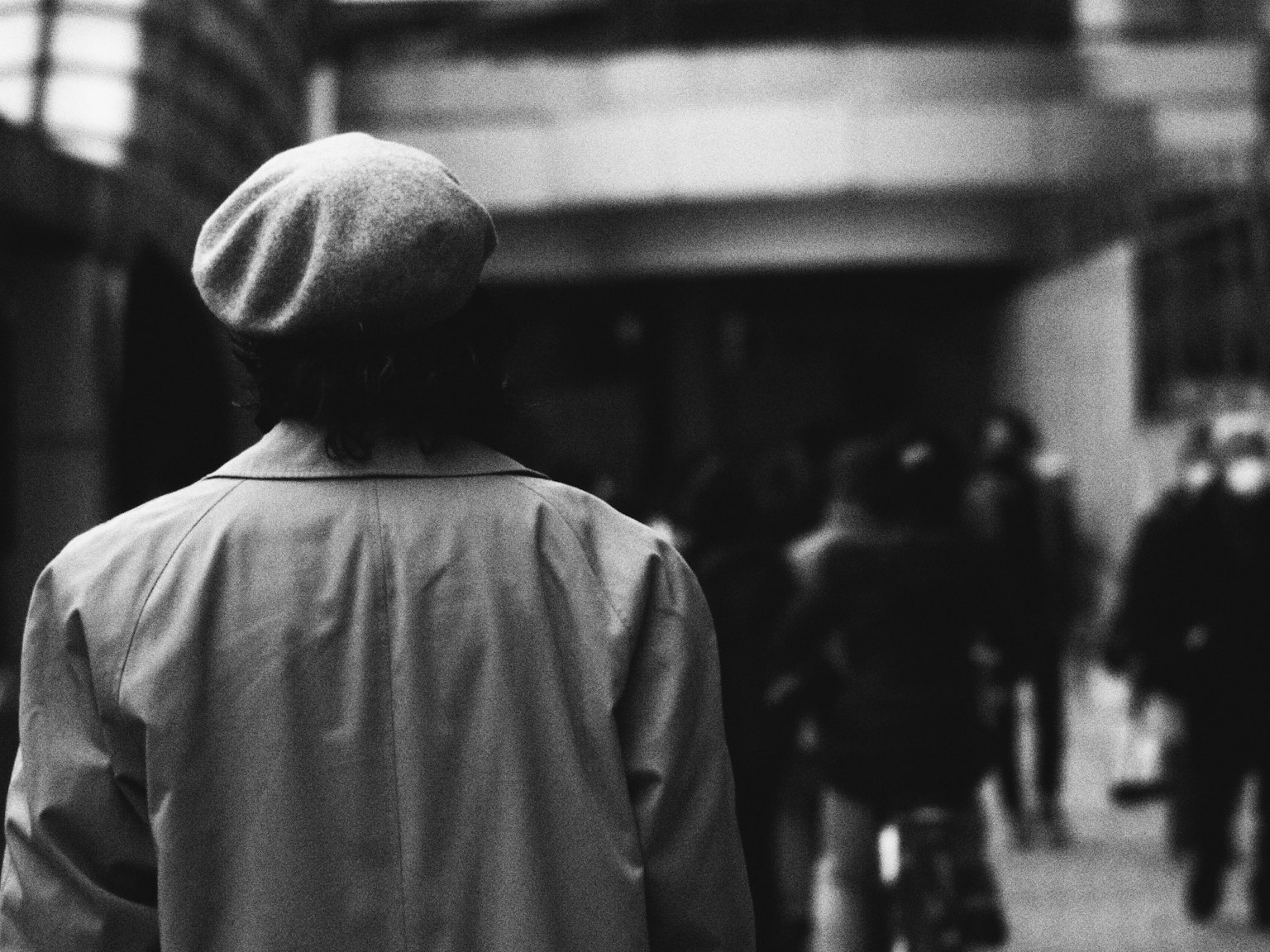 Una persona con un berretto che cammina in una scena di strada in bianco e nero