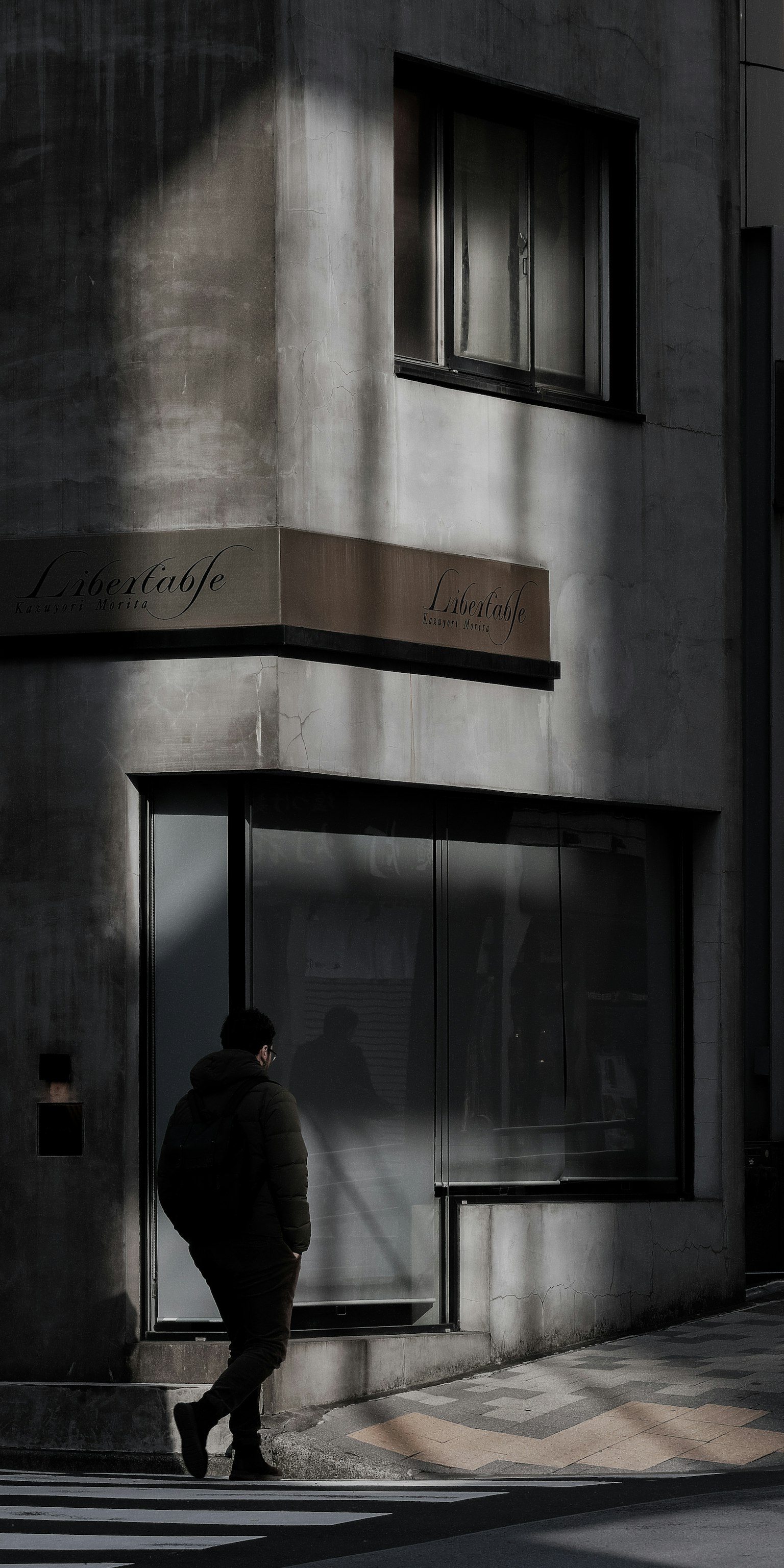 Silhouette of a person walking at a street corner with shadows and modern building facade