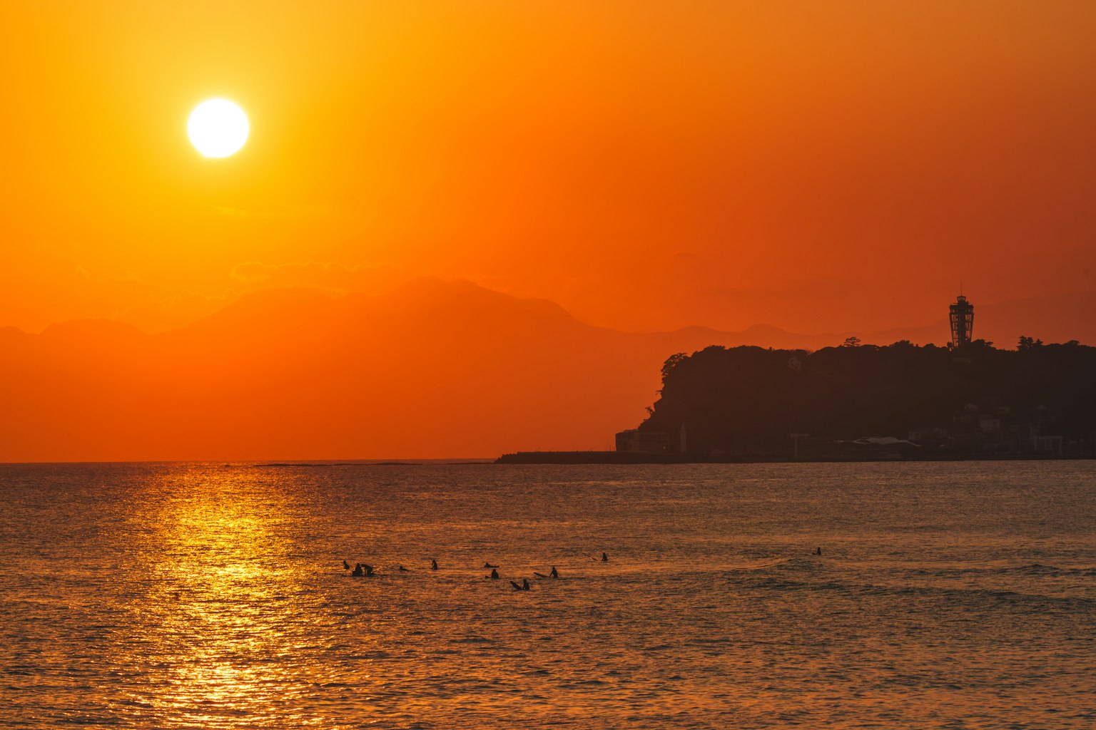 Un impresionante atardecer sobre el océano con surfistas y un faro al fondo