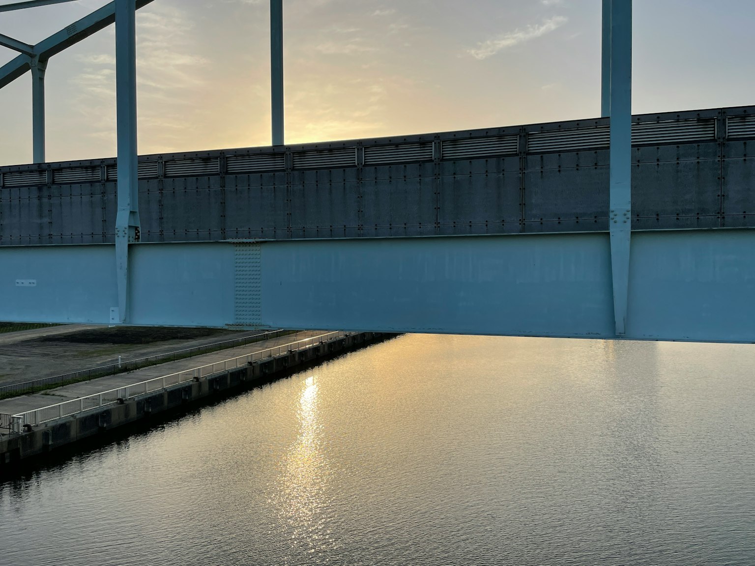A blue bridge reflecting on the water with a sunset in the background