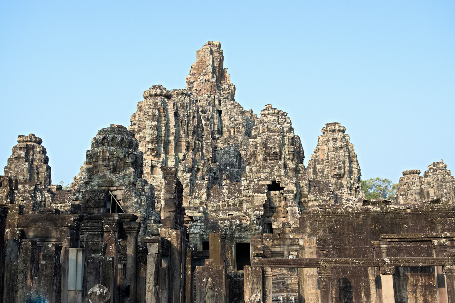 Menara batu yang khas dari Kuil Bayon di Angkor Wat menjulang di latar belakang langit biru