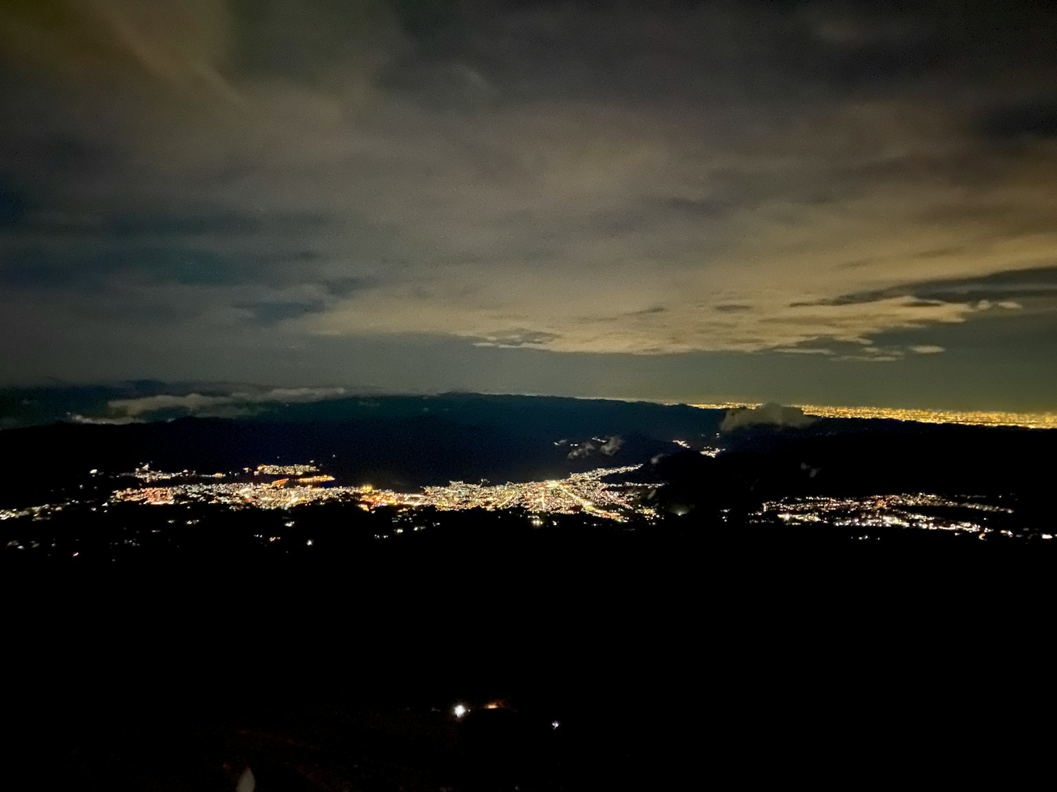 Vista nocturna de un horizonte urbano con luces dispersas y cielo nublado