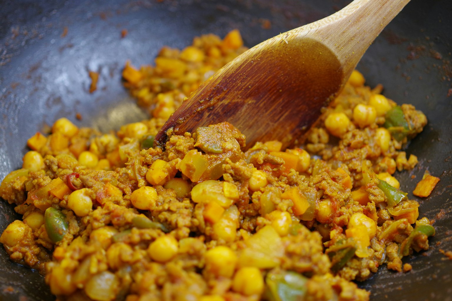 Remuant du riz jaune et des légumes dans une poêle avec une cuillère en bois