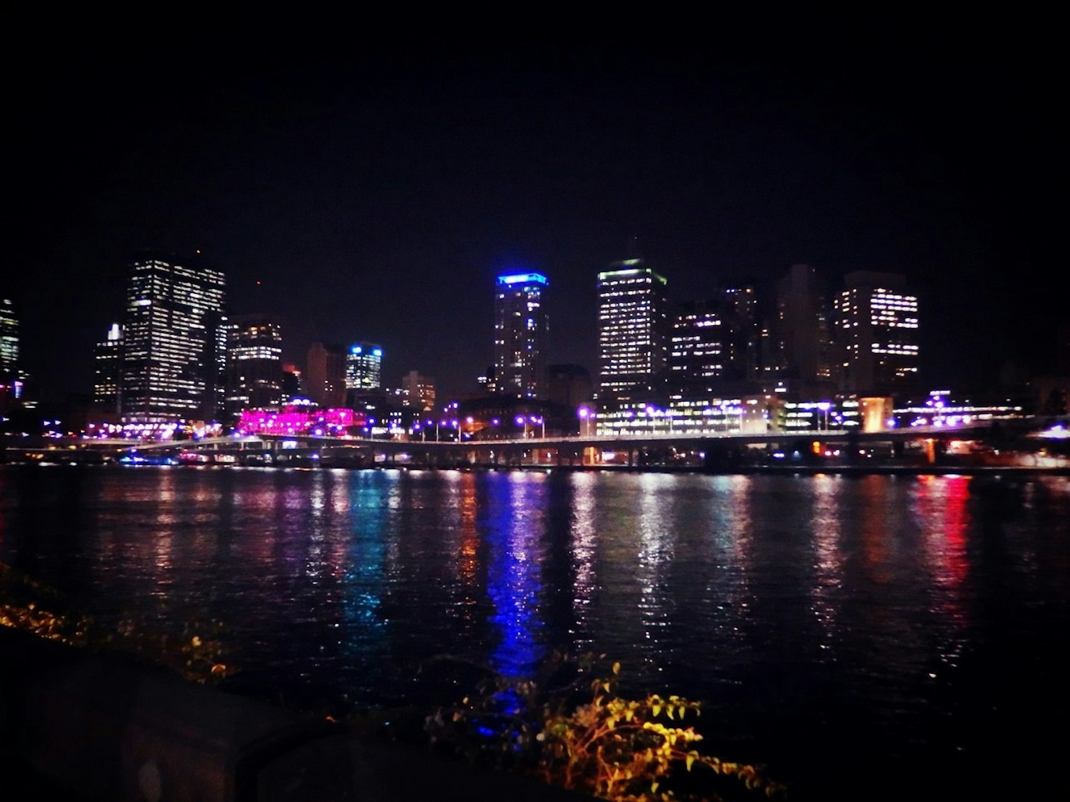 Vista nocturna de un horizonte urbano con luces coloridas reflejándose en el río