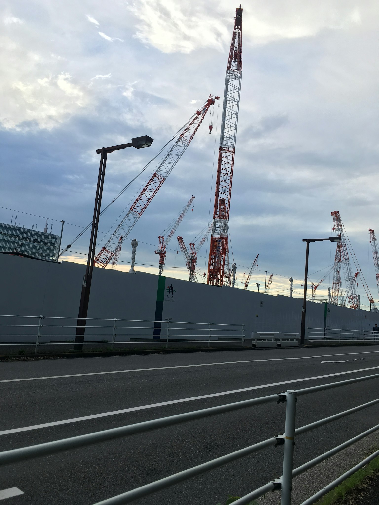 Cantiere con gru e muro grigio lungo una strada