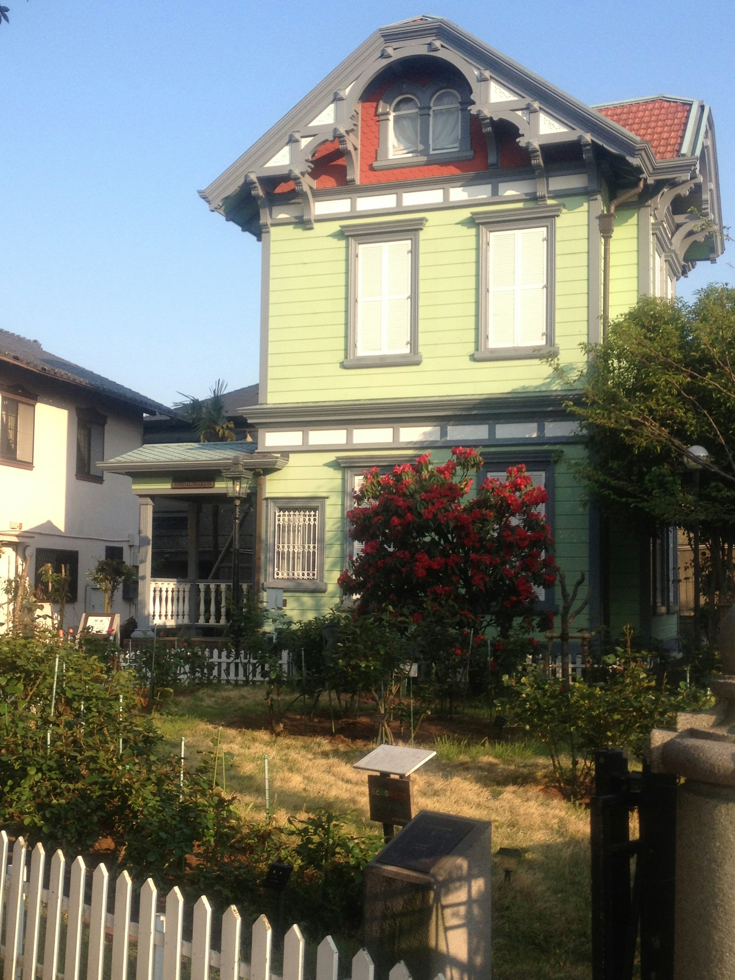 緑の外壁の一戸建て住宅と庭の花が見える戸外の風景