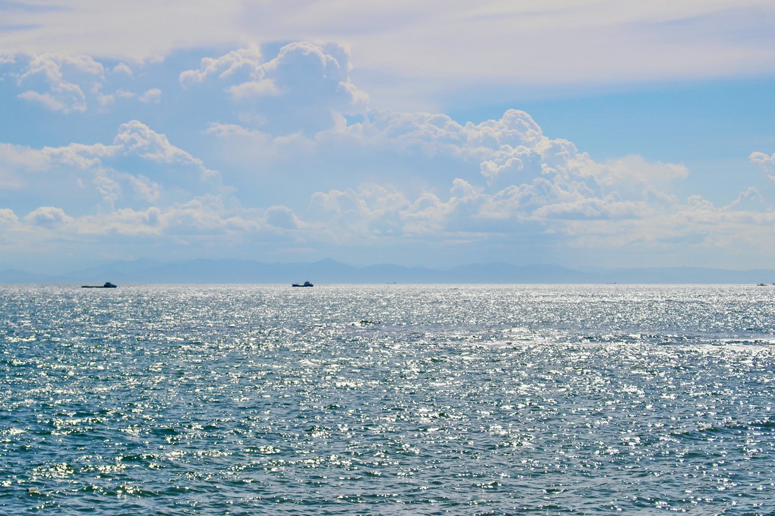 A serene seascape with shimmering blue water and distant boats under a cloudy sky