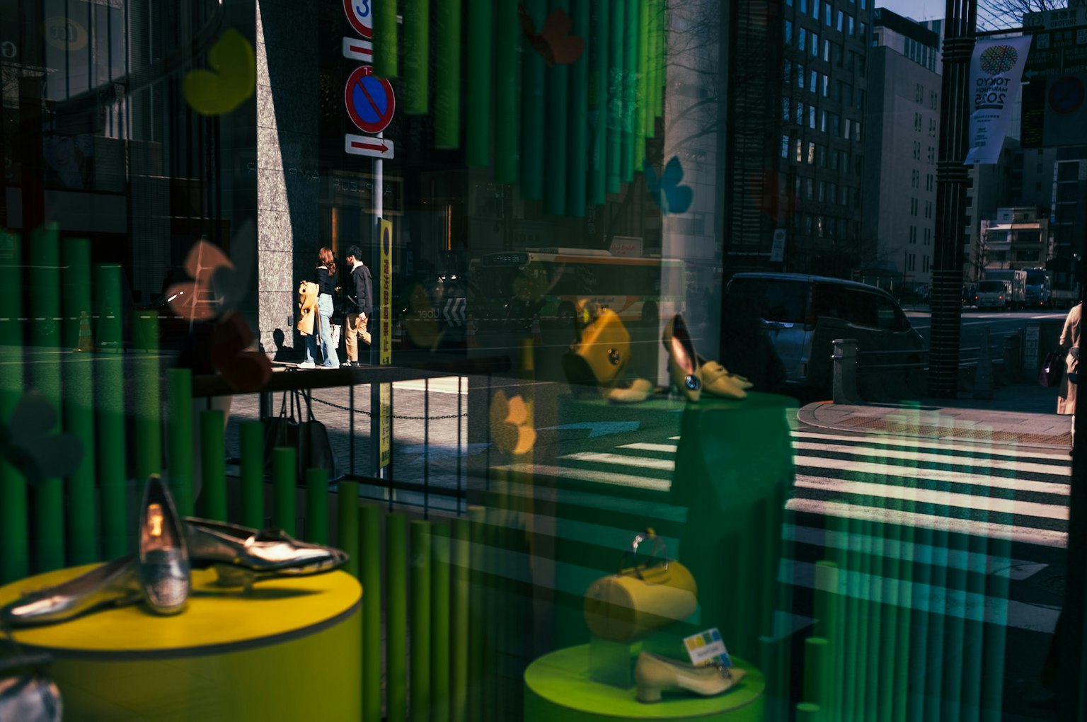 Imagen de una vitrina reflejando una escena de ciudad mesas amarillas y zapatos visibles