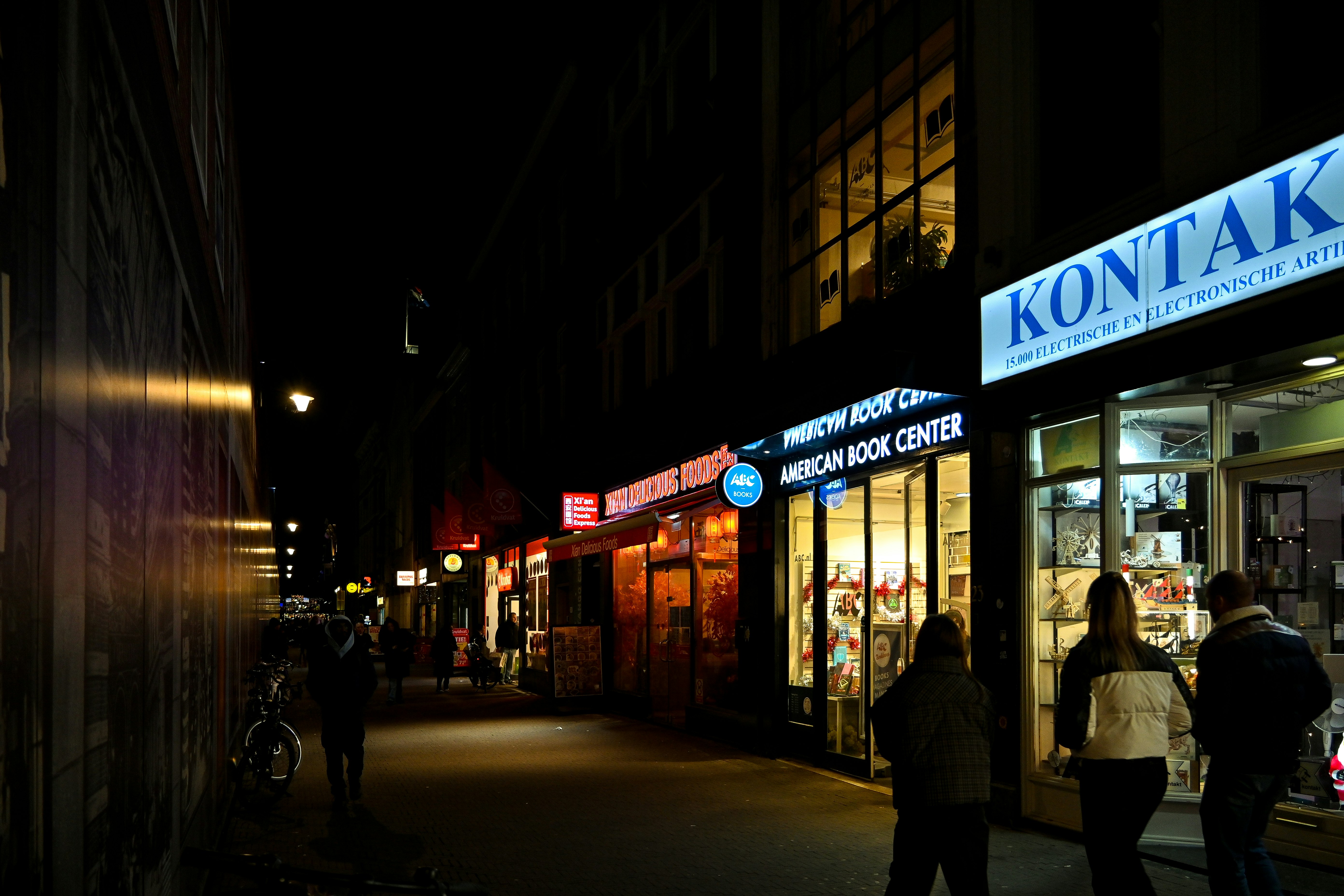 มุมถนนยามค่ำคืนพร้อมป้ายร้านหนังสือและเงาคน