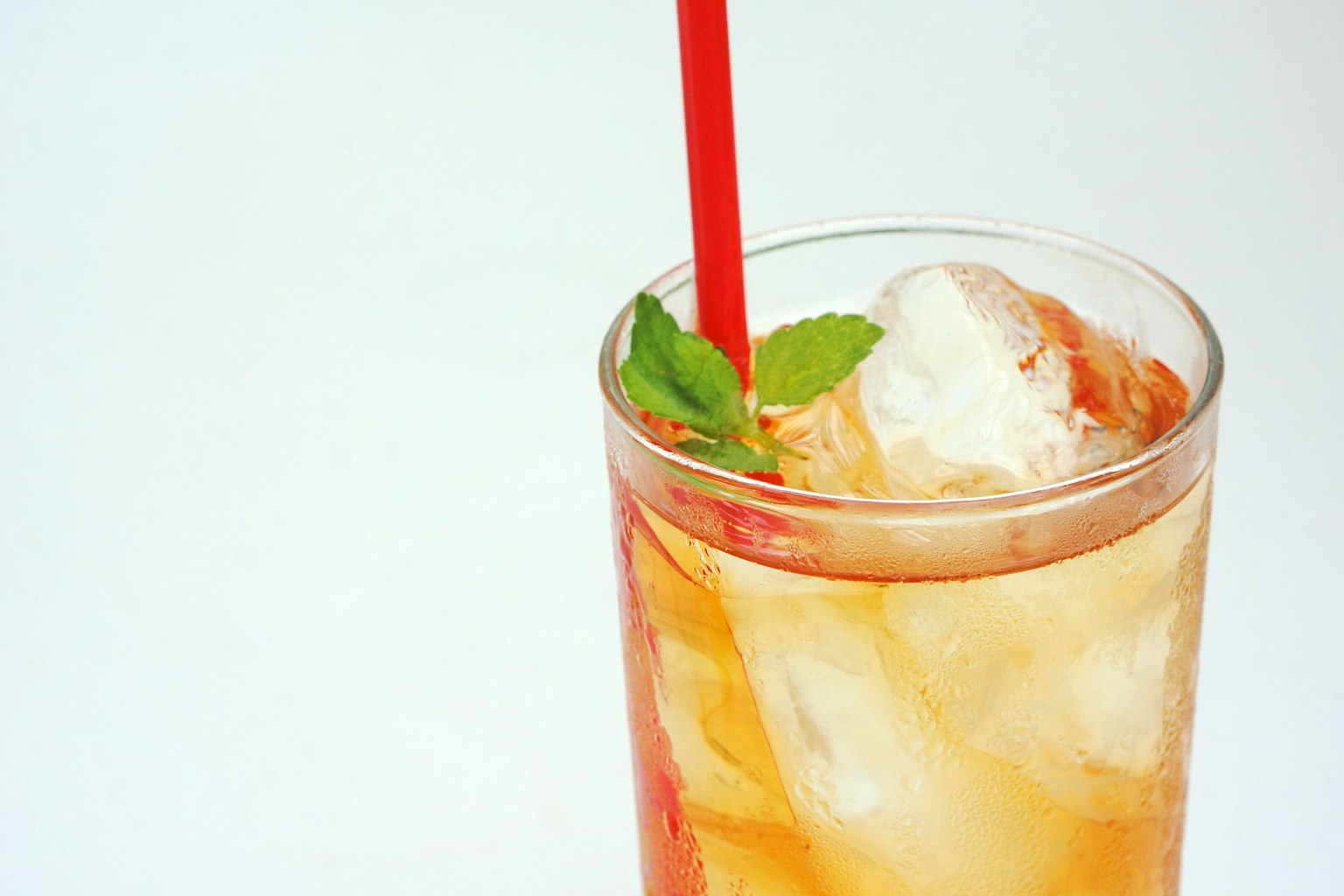 Segelas minuman es dengan sedotan merah dan sehelai daun mint