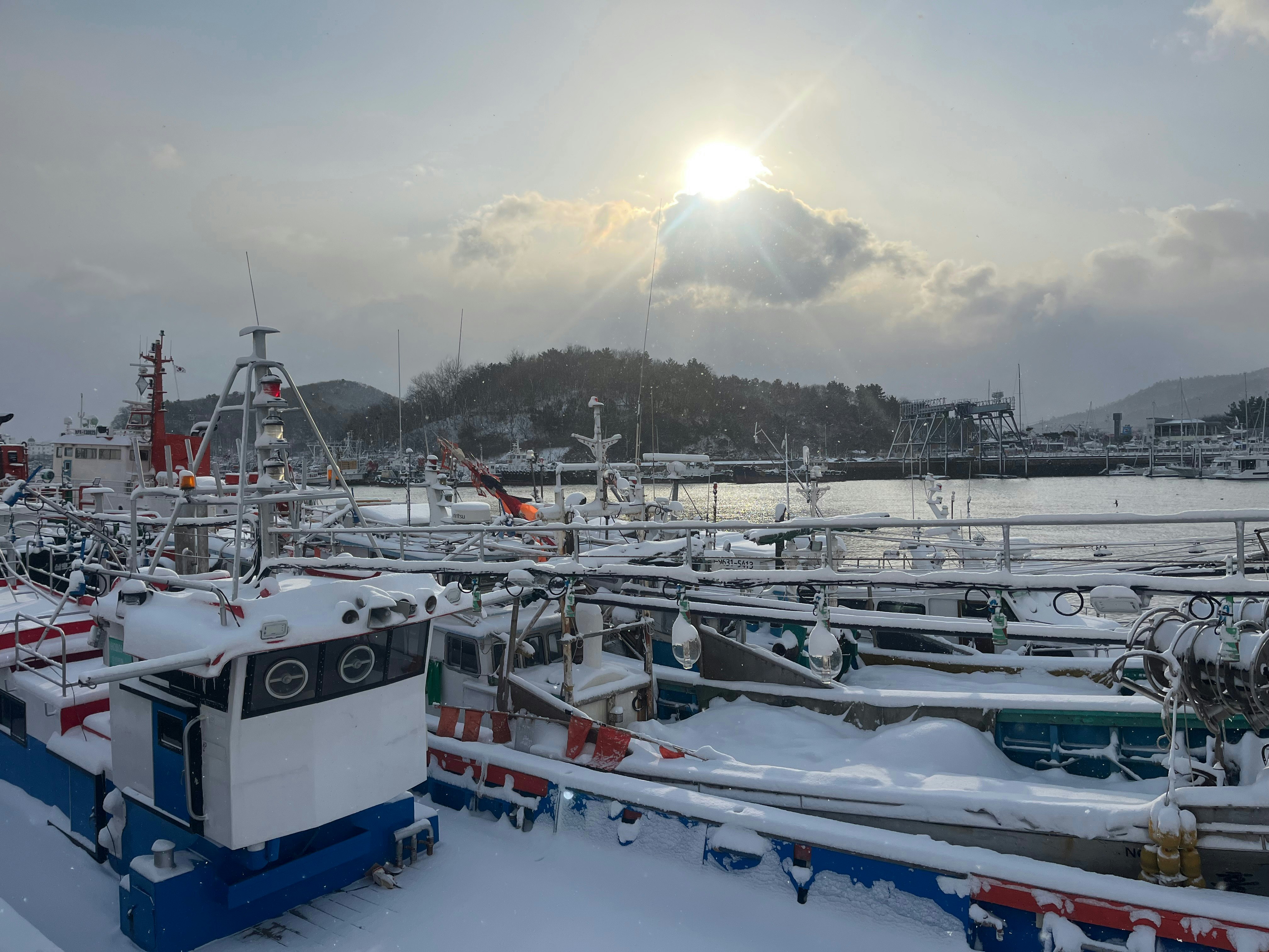 verschneiter Hafen mit festgemachten Booten und Kränen am Kai