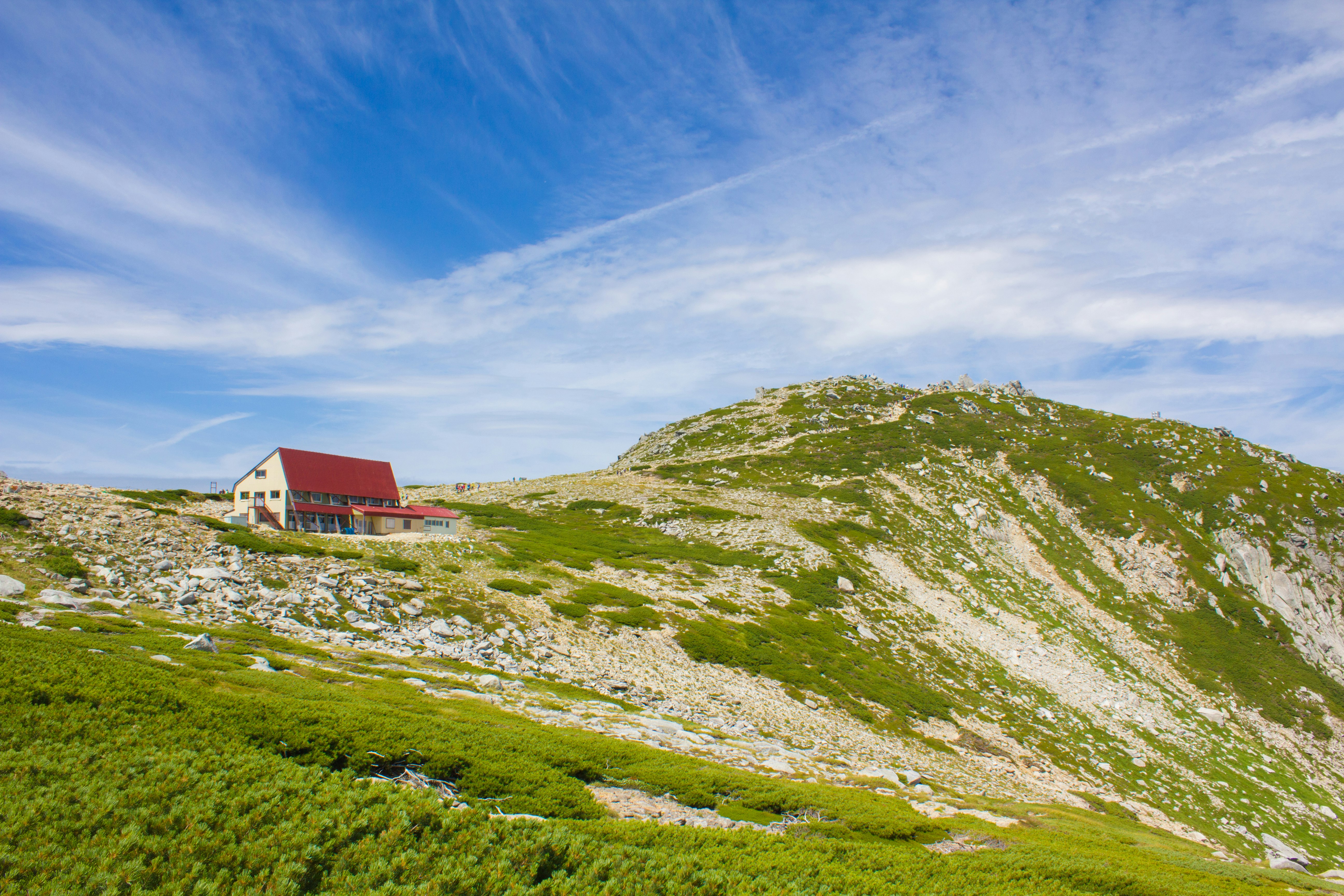 rotes Bergrefugium auf einer grünen Bergkuppe unter blauem Himmel