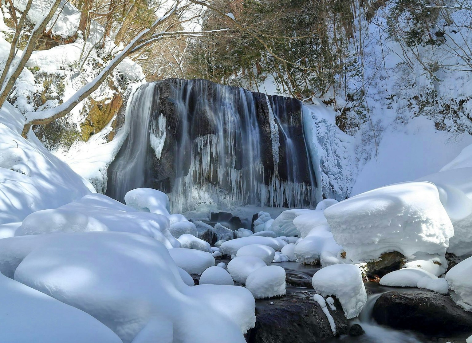 Air terjun beku dikelilingi salju dan batu
