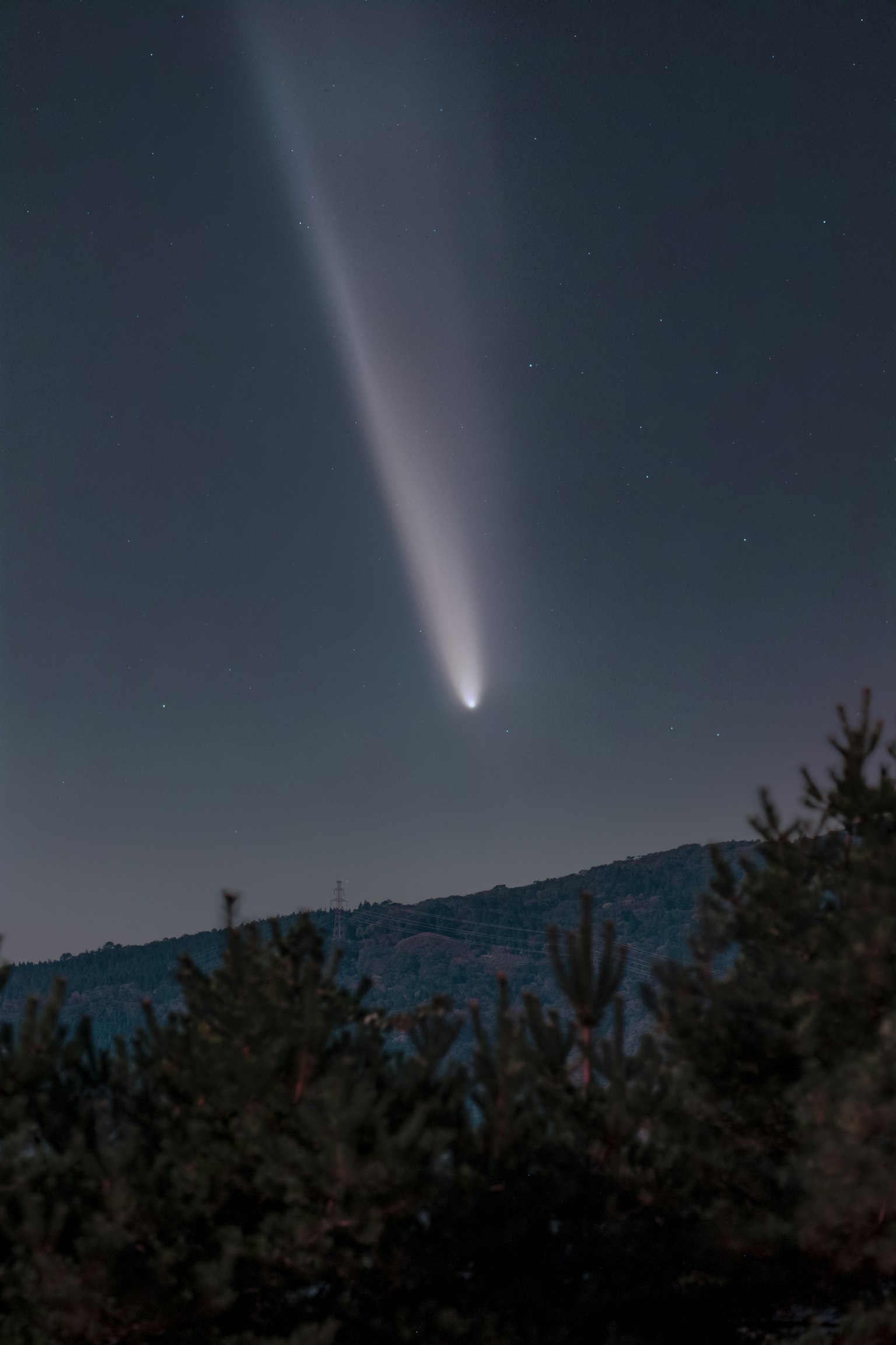 A comet shining in the night sky above a mountain silhouette