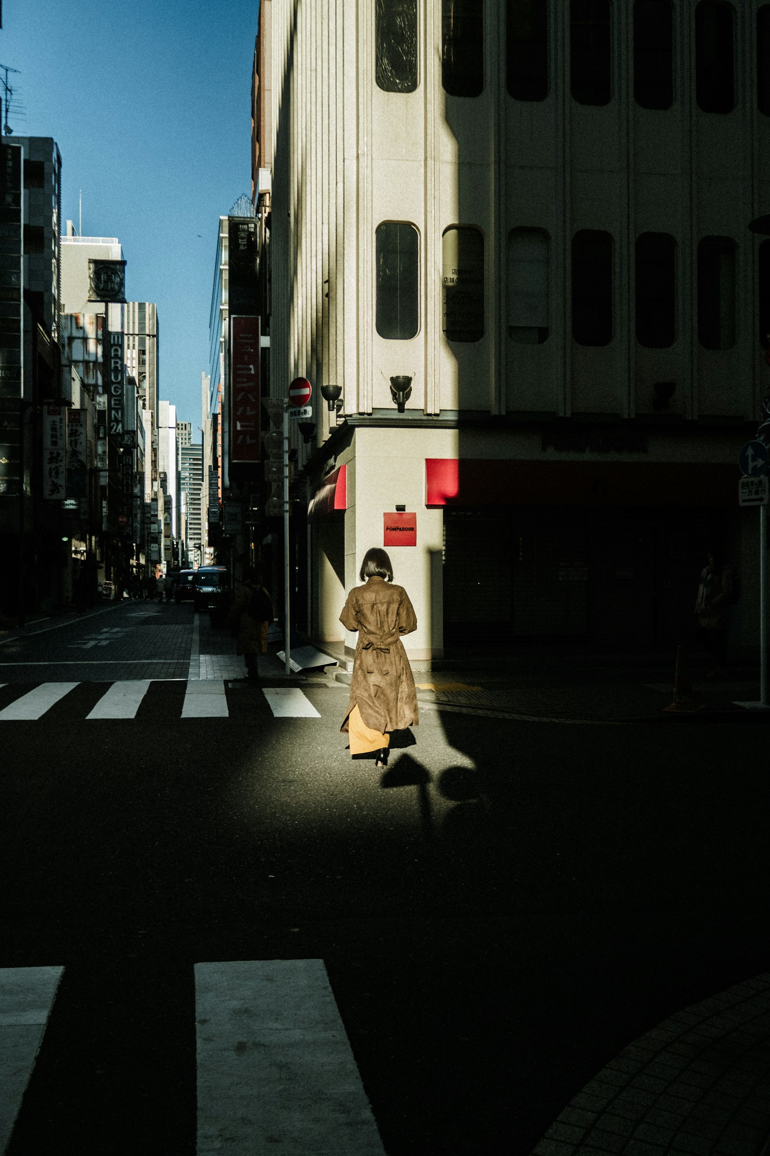 A woman walking in shadows at a street intersection with contrasting light and shadow