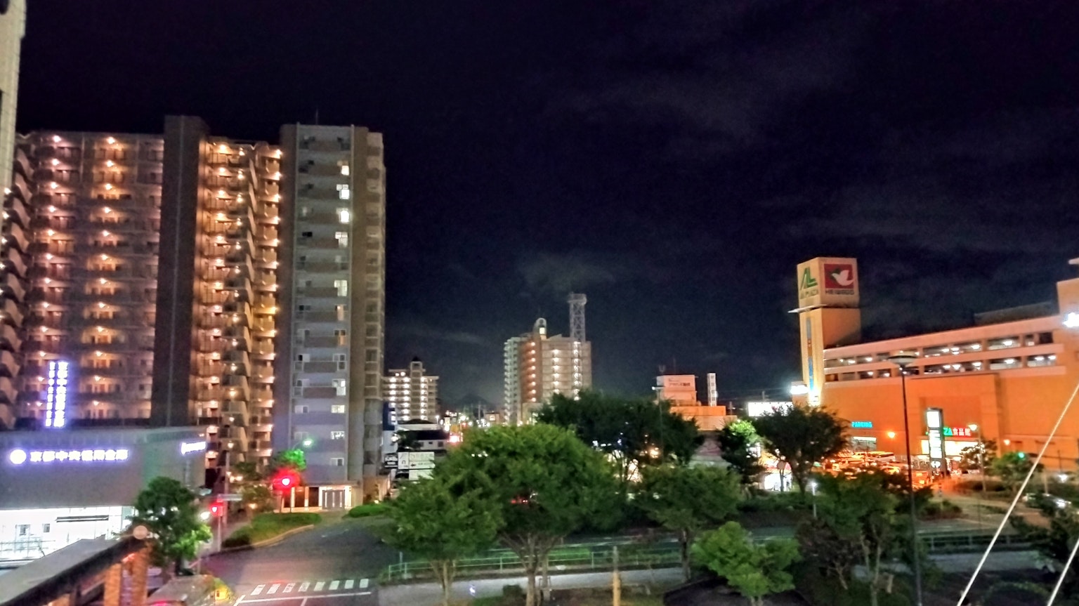 Pemandangan kota malam dengan gedung tinggi dan pohon hijau di bawah langit gelap