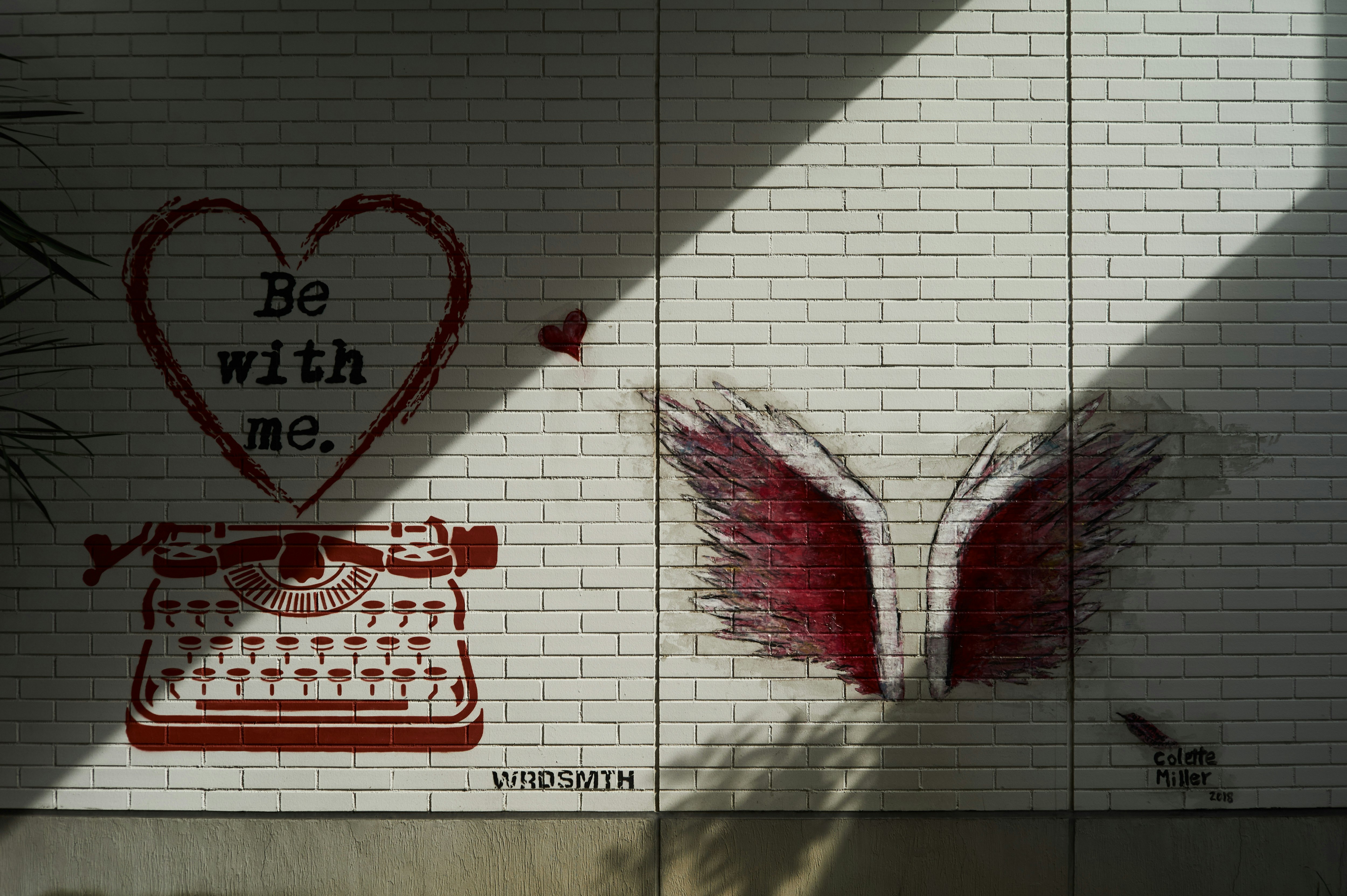 Graffiti-Wand mit Herzformen und geflügeltem Motiv im Sonnenlicht und Schatten