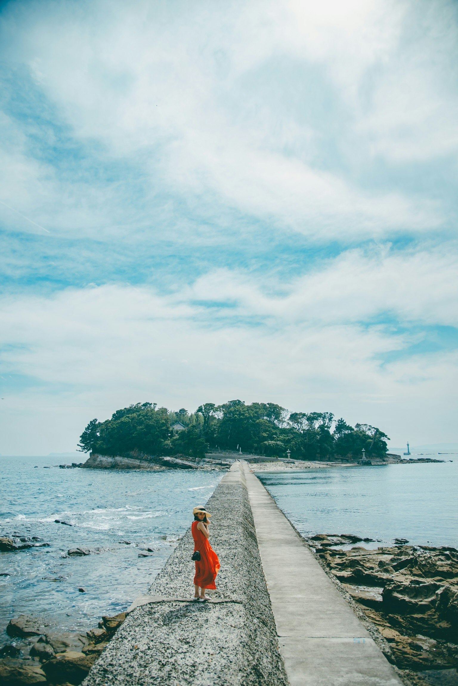 A woman in a red dress standing on a stone pathway leading to an island