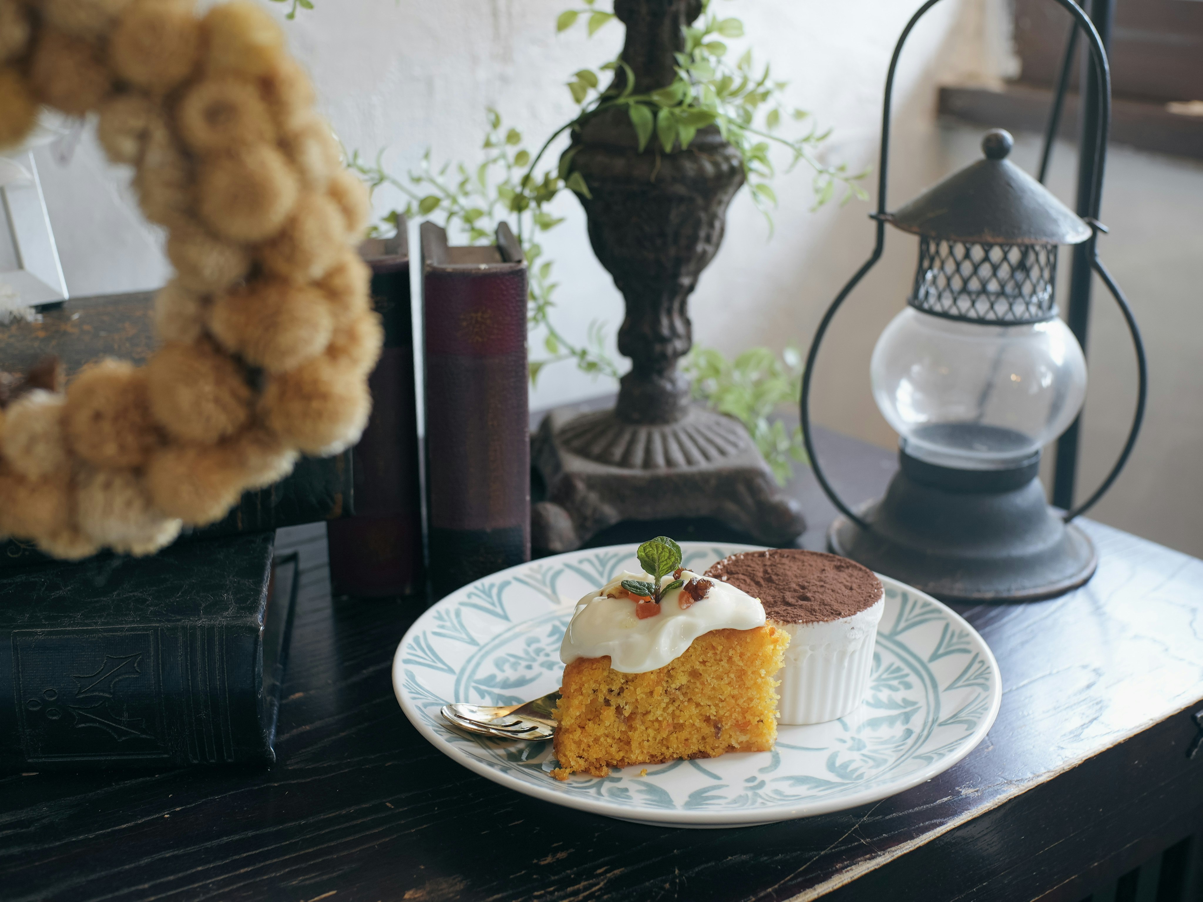 花柄皿にのったケーキとミニランプのある室内カフェ風テーブル